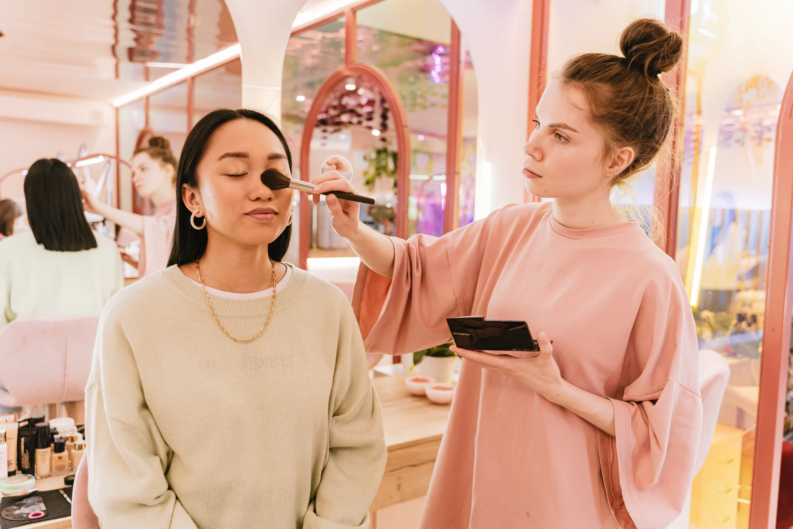 A makeup artist applying blush to a client's face in a brightly lit salon setting.