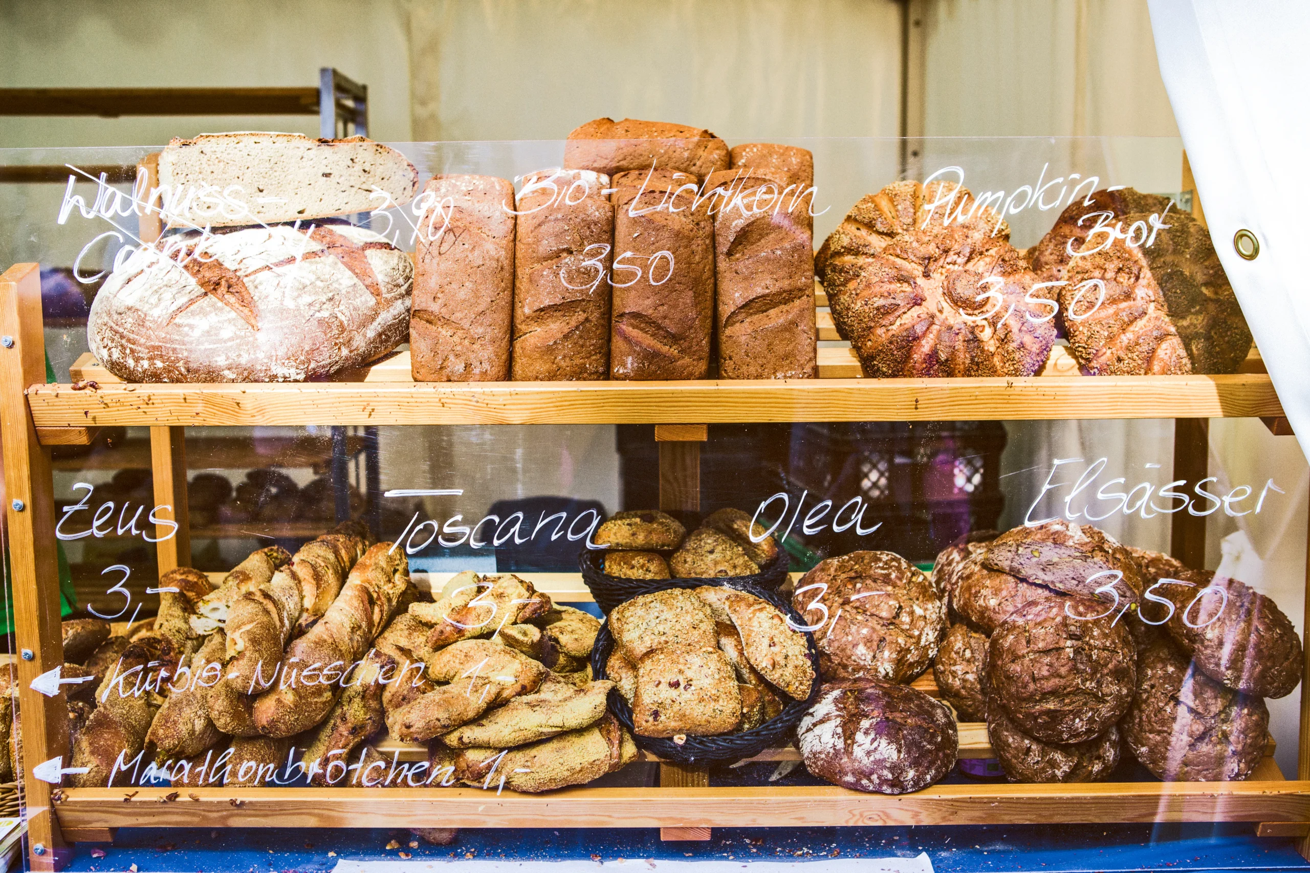 A bakery display case showcasing a variety of artisan breads with handwritten labels and prices.