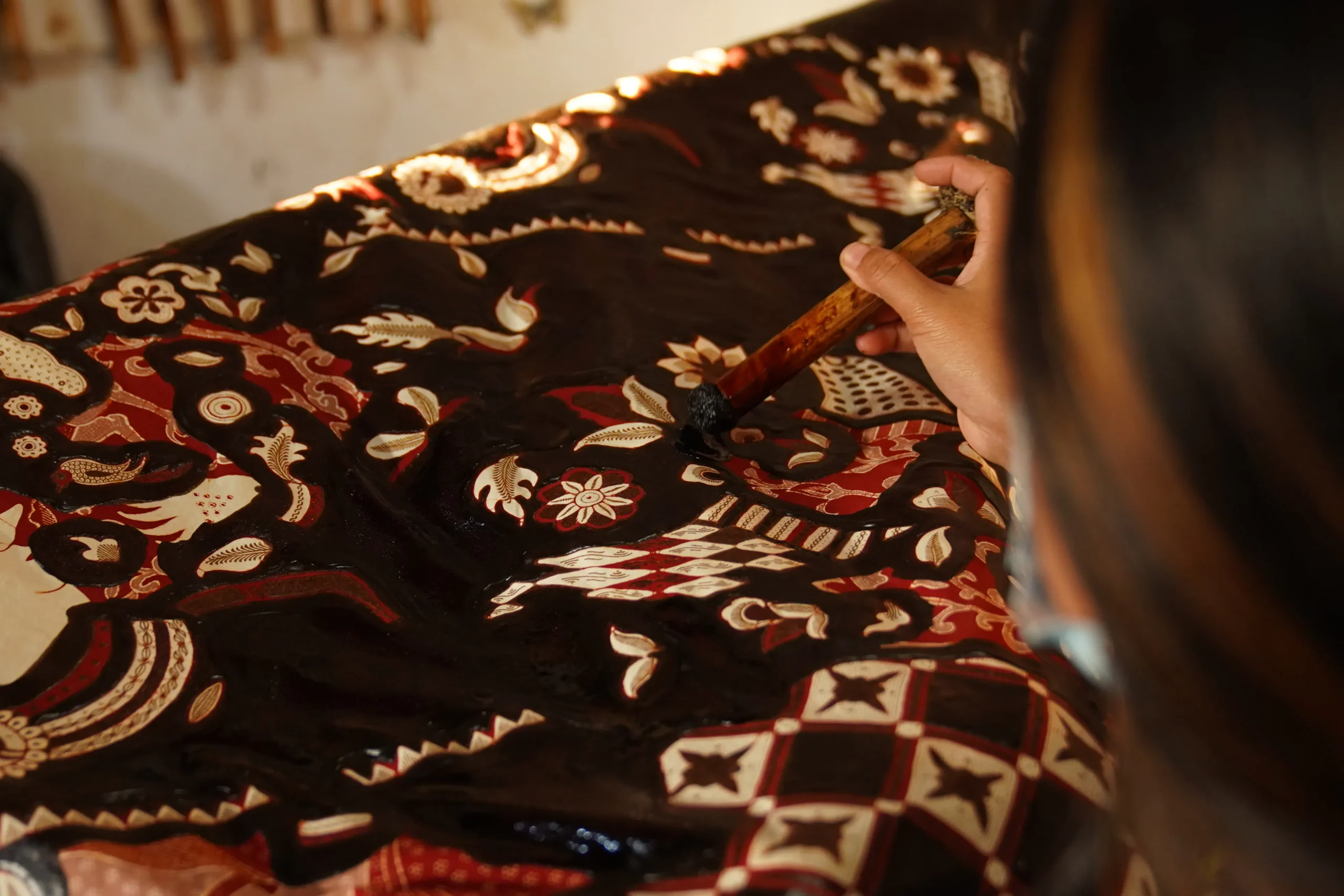 Person painting intricate floral and geometric designs on dark brown fabric with dye.