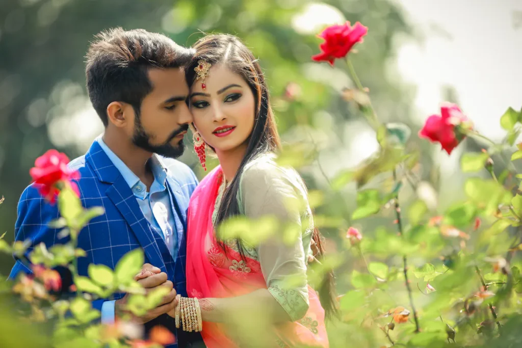 Couple embracing among roses, woman in traditional dress with jewelry.