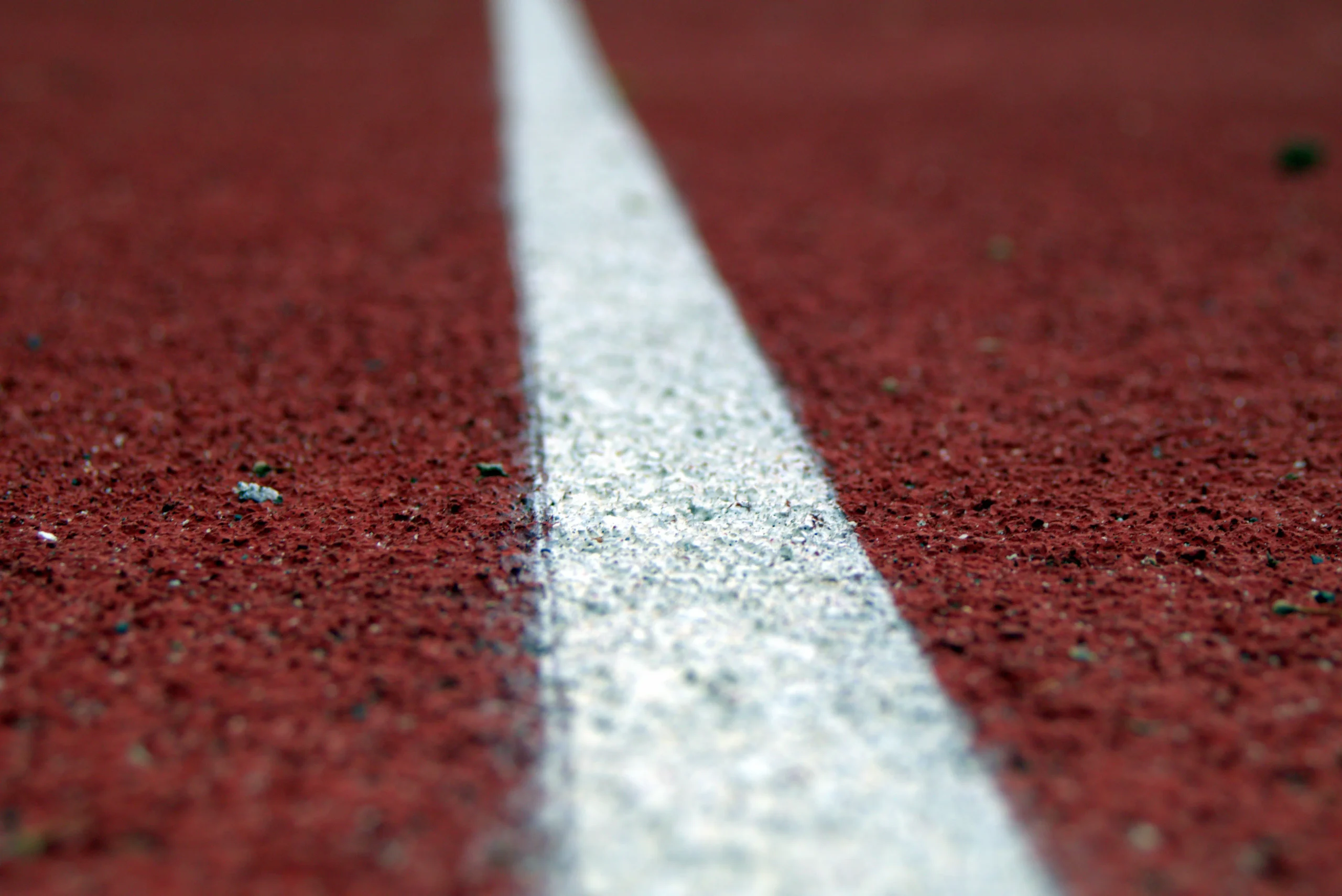 A close-up shot of a white line marking on a red running track, symbolizing boundaries and direction.