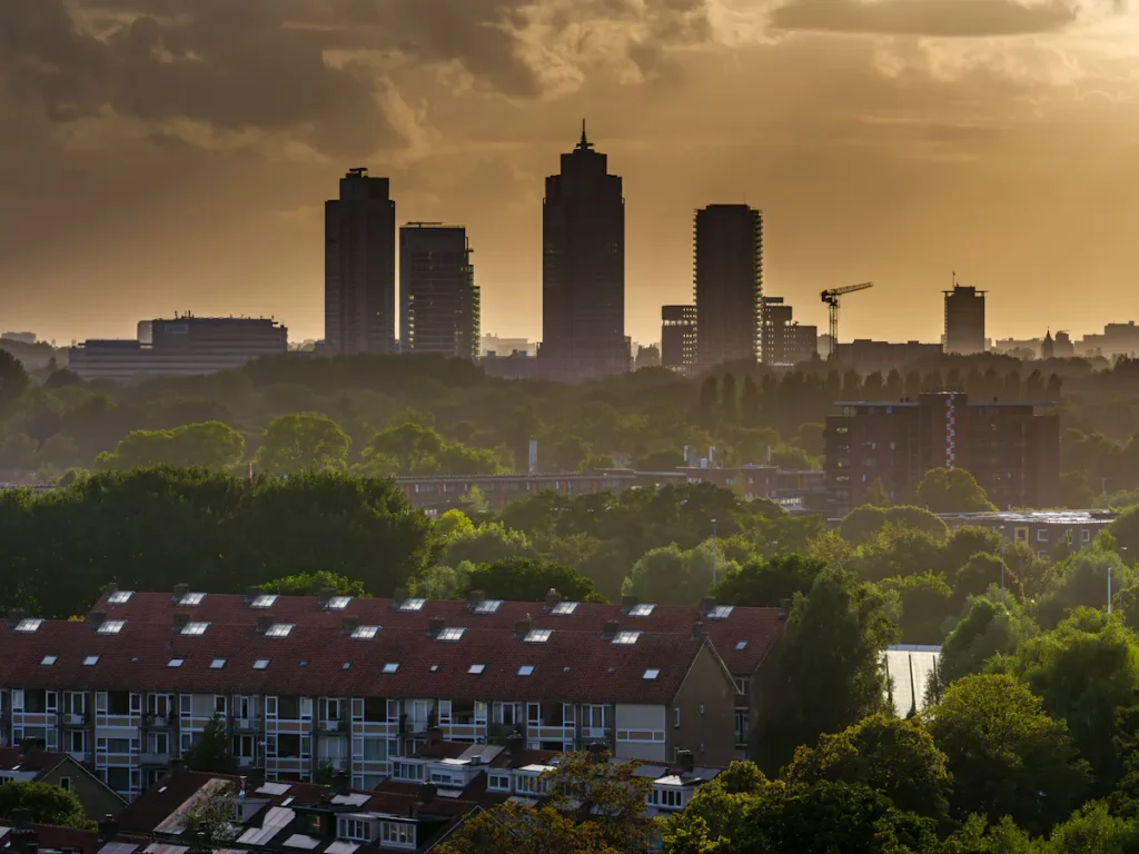 Amsterdam skyline at dusk with high-rise buildings and warm, cloudy sky.