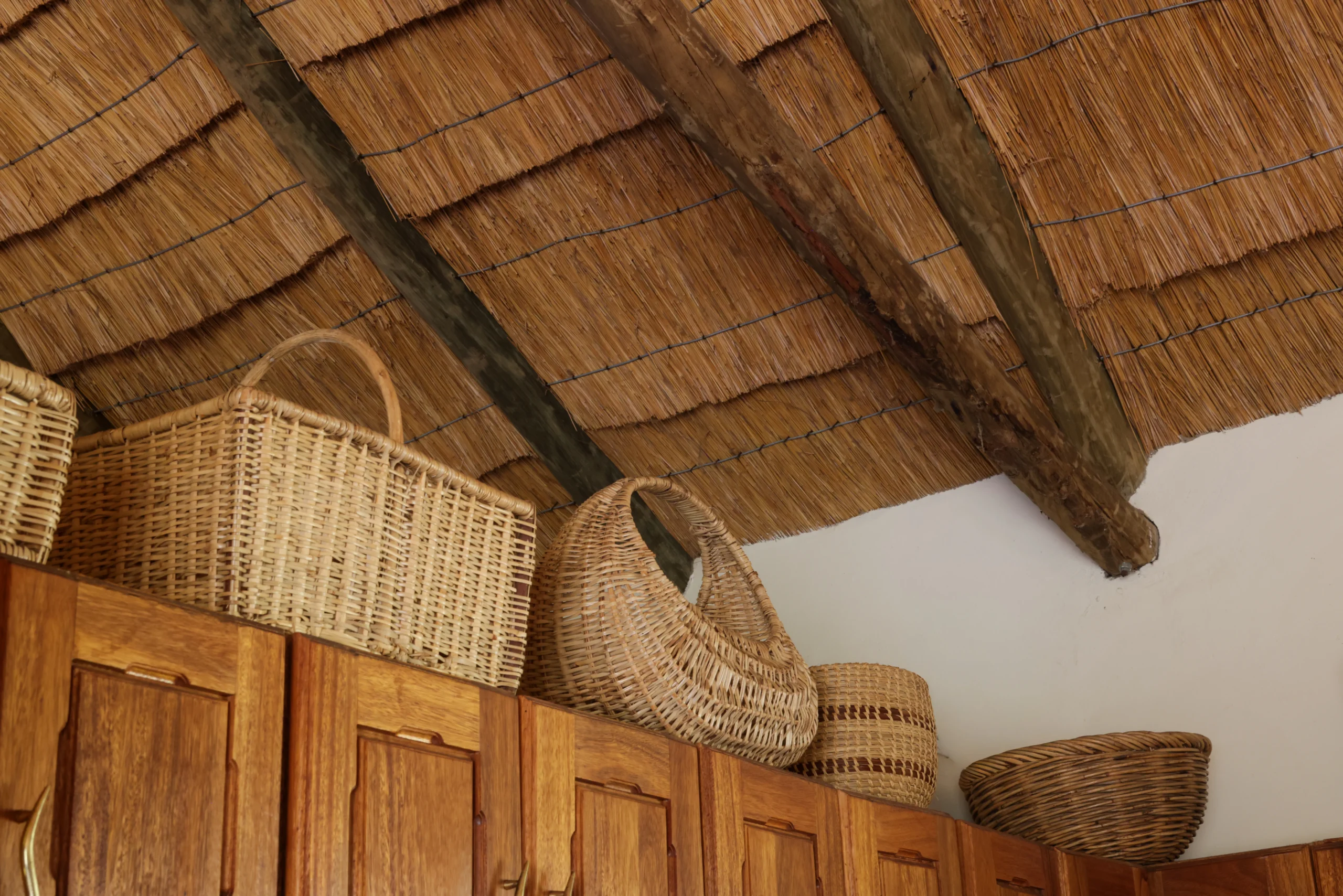 Wicker baskets on top of wooden cabinets, straw ceiling.