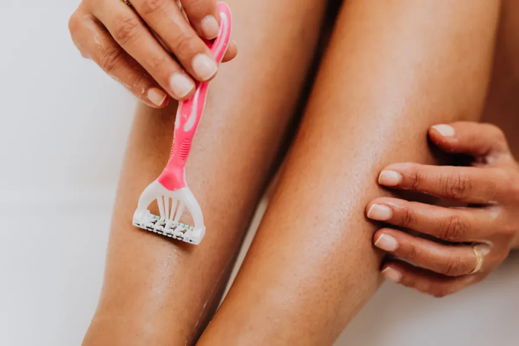 Close-up of person shaving their leg with pink razor for hair removal
