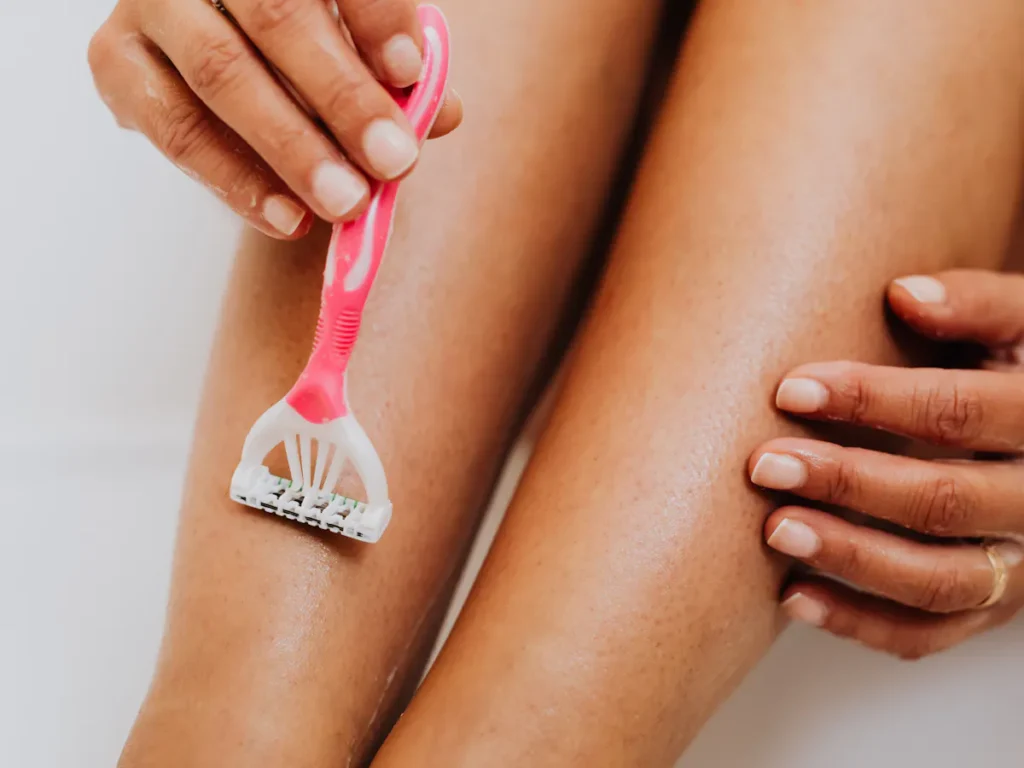 Close-up of a woman shaving her legs for smooth skin, an alternative to laser waxing for hair removal.