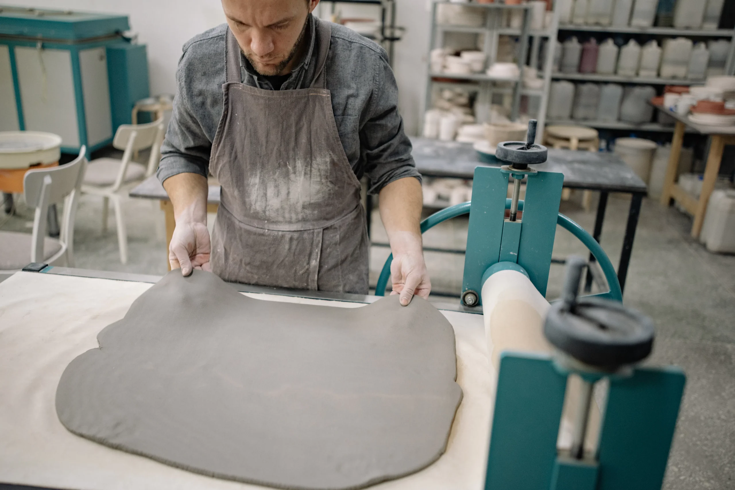 Man in apron smoothing gray clay on a table in a workshop.