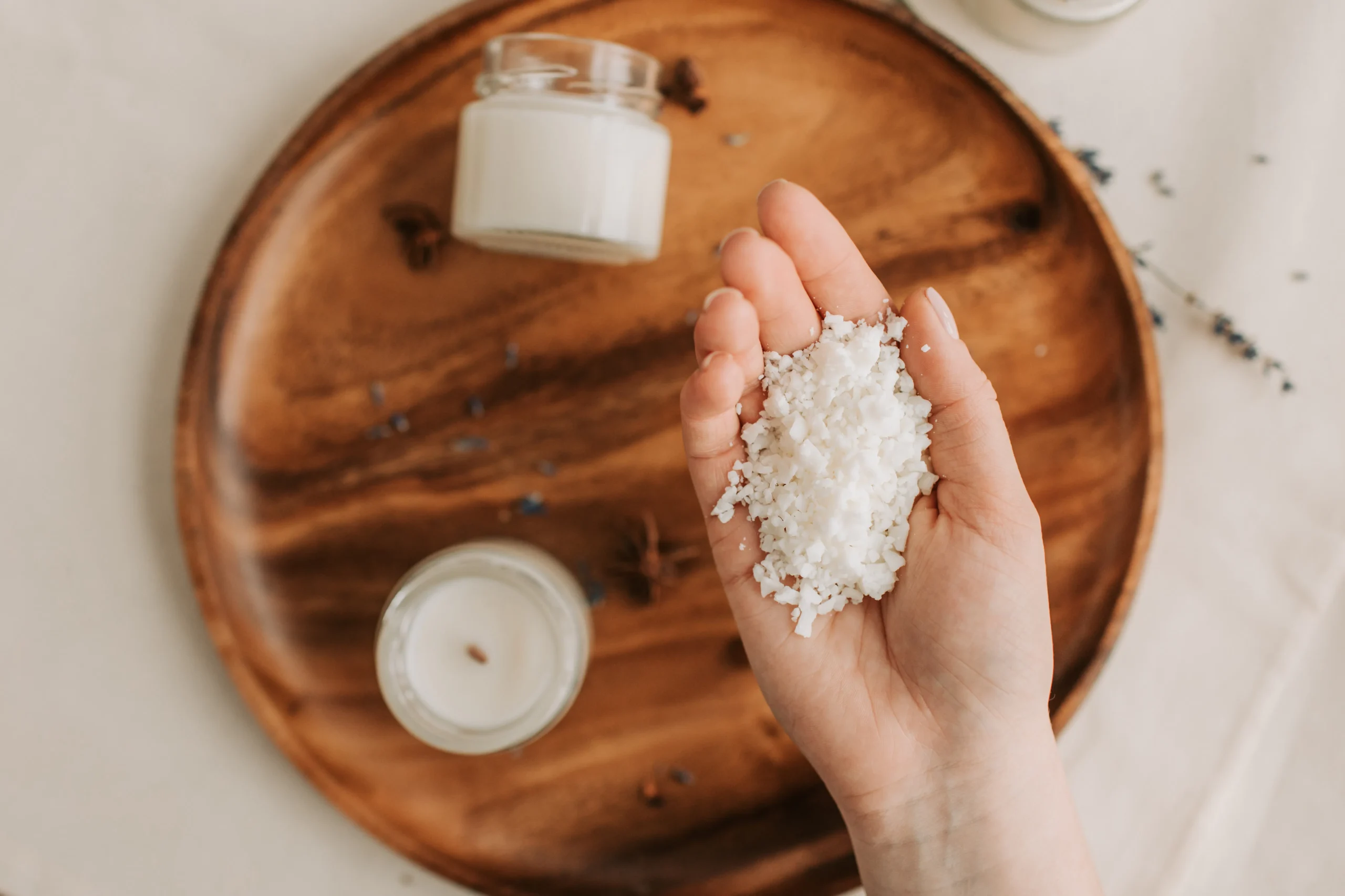 Close-up overhead shot of a hand holding sea salt on a wooden plate surrounded by candles, creating a spa-like ambiance.