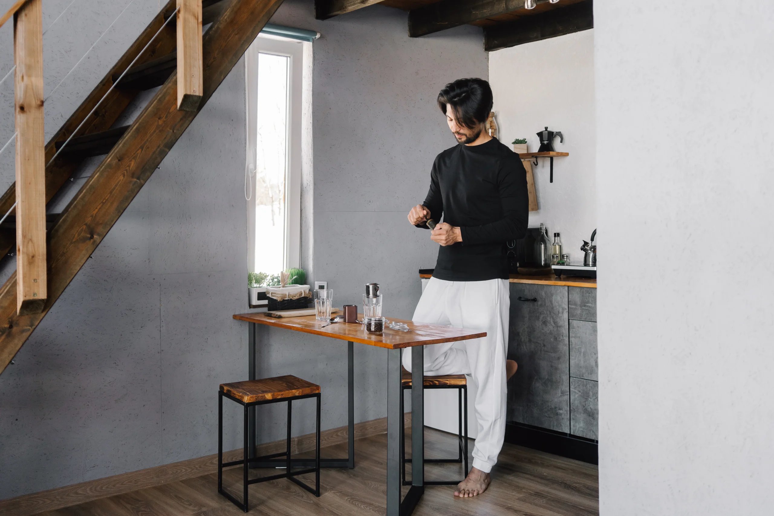 Man in black shirt standing in a modern kitchen preparing coffee.