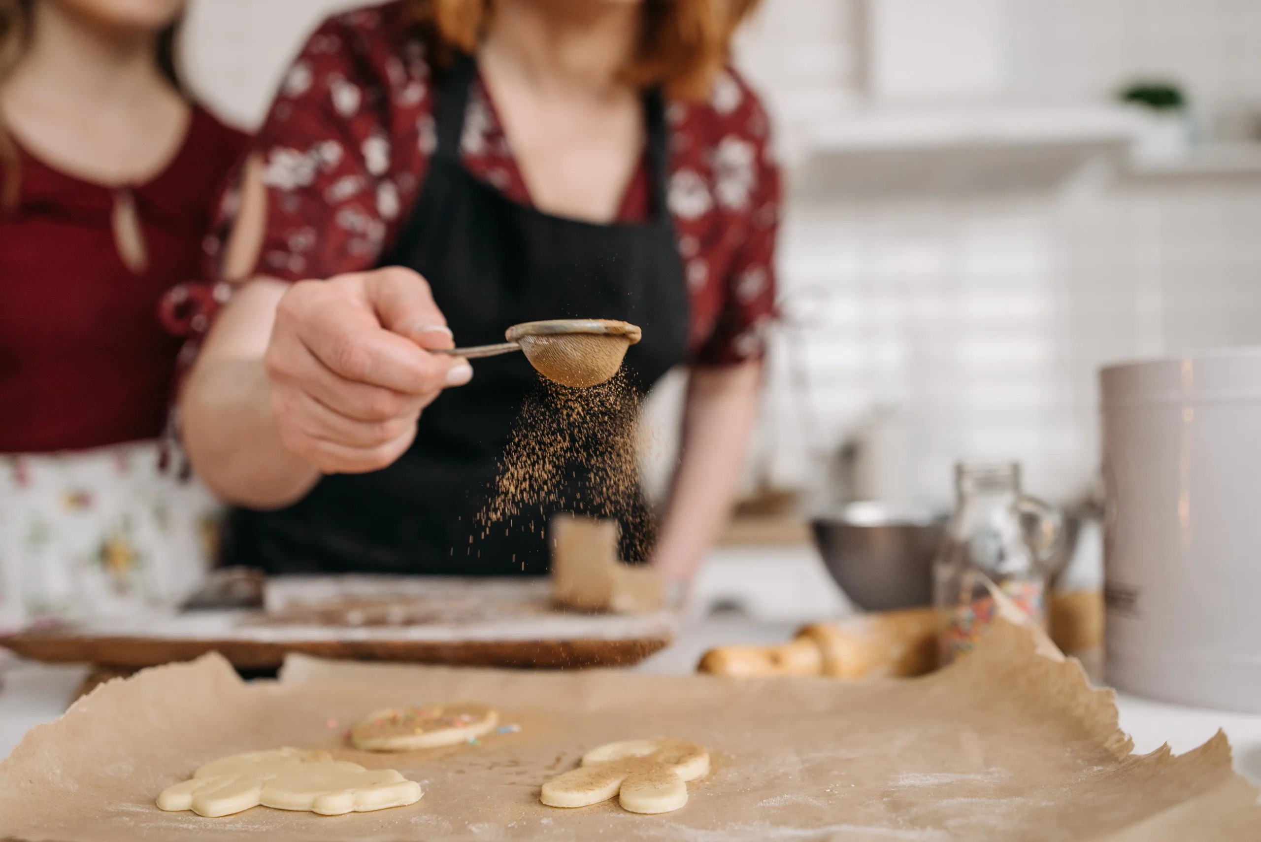 Woman sifting spices onto cookies, baking in kitchen, close-up of hand.
