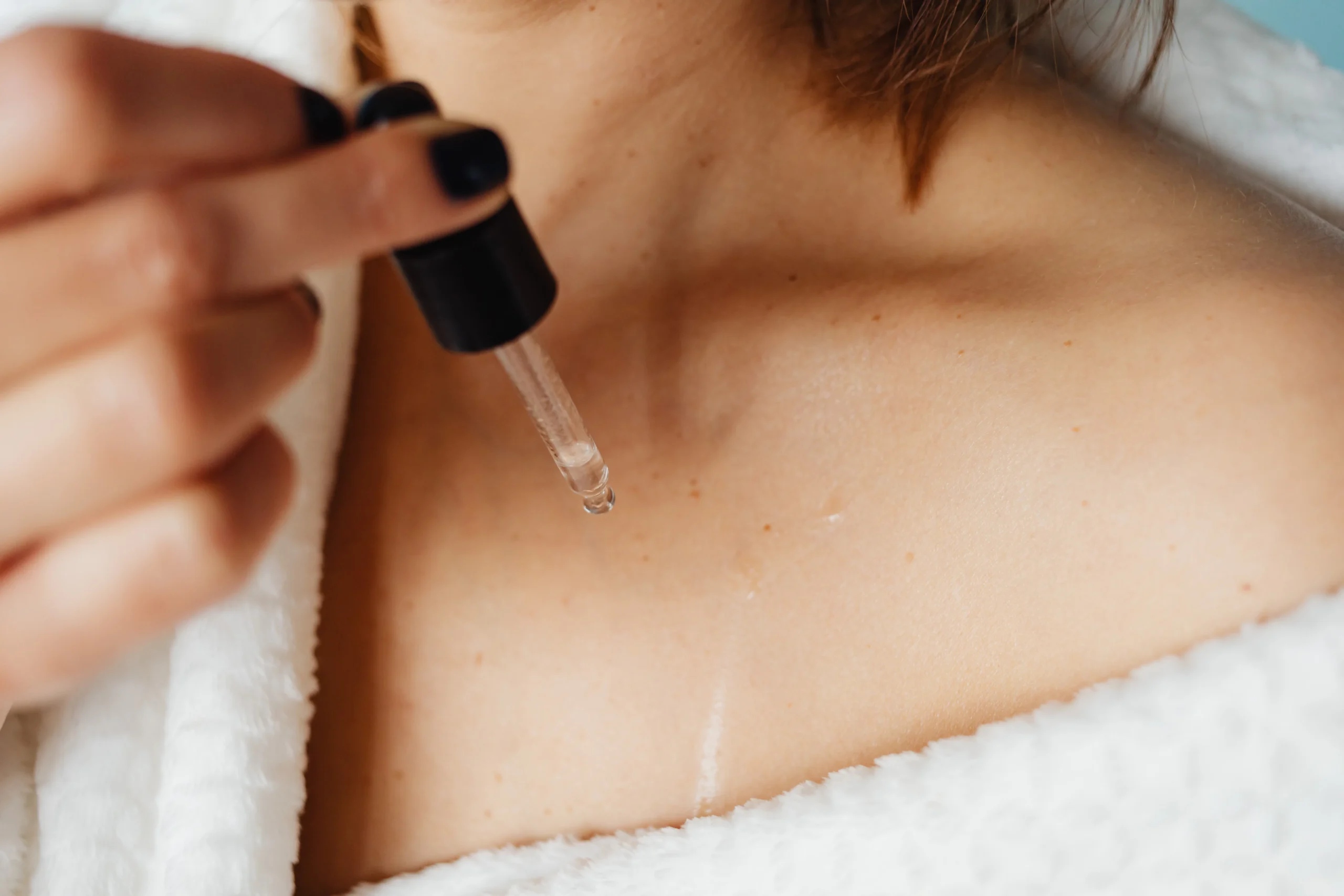 A woman applying serum to her skin, possibly as part of a skincare routine to maintain smooth skin after hair removal methods like laser waxing.