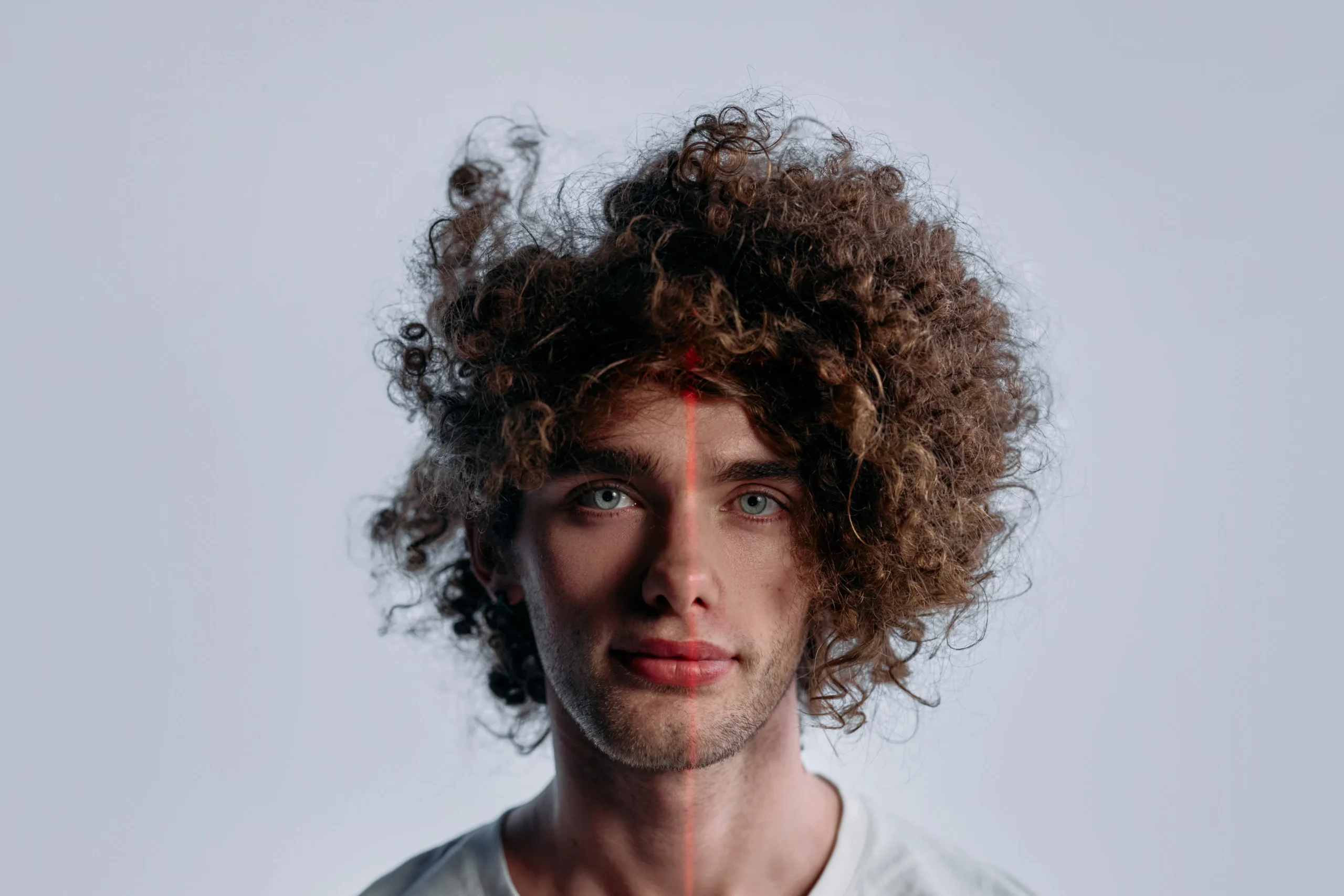 Man with curly hair and red laser line on face for facial laser treatment.
