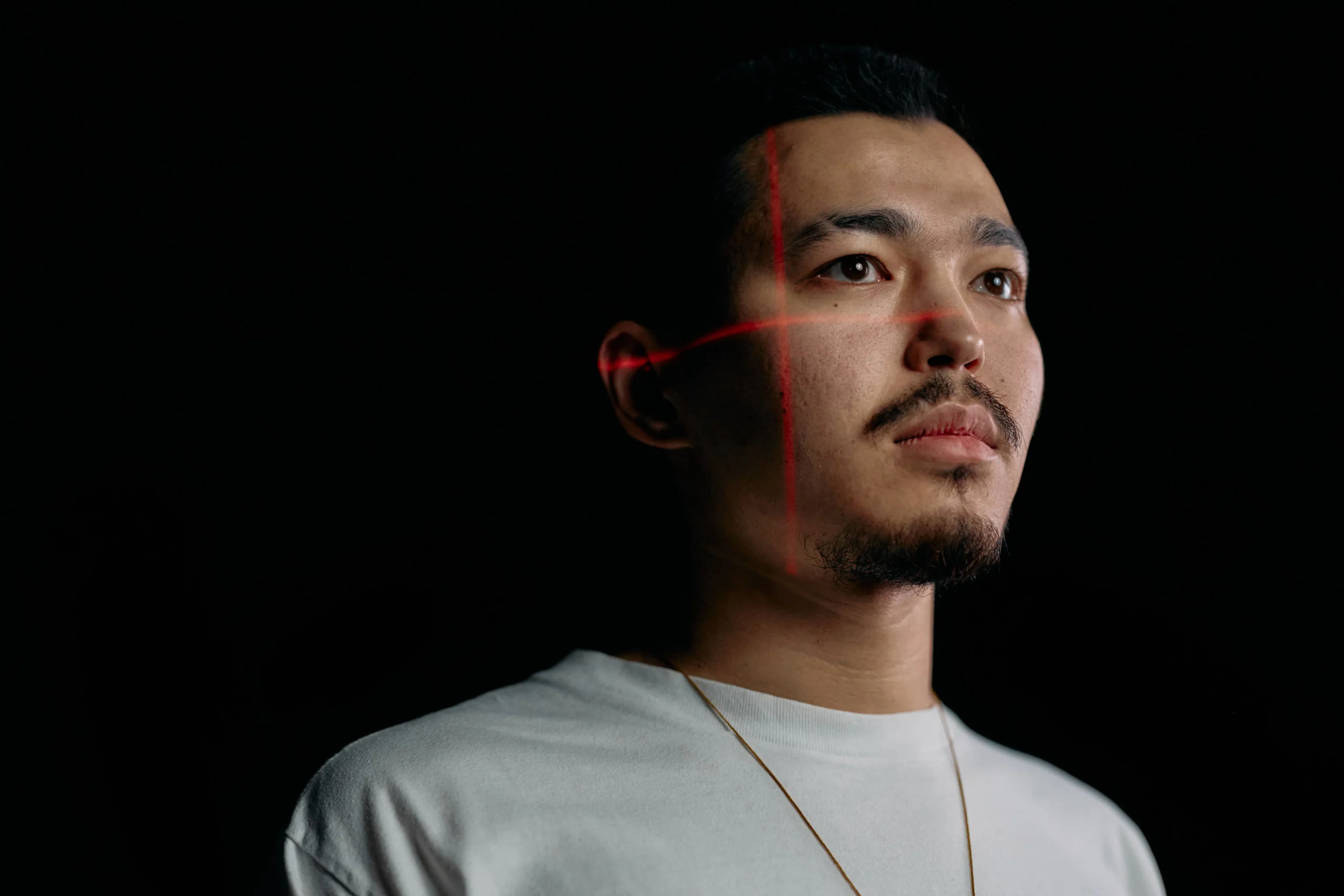 Close-up of man's face with red laser lines, possibly undergoing laser hair removal.