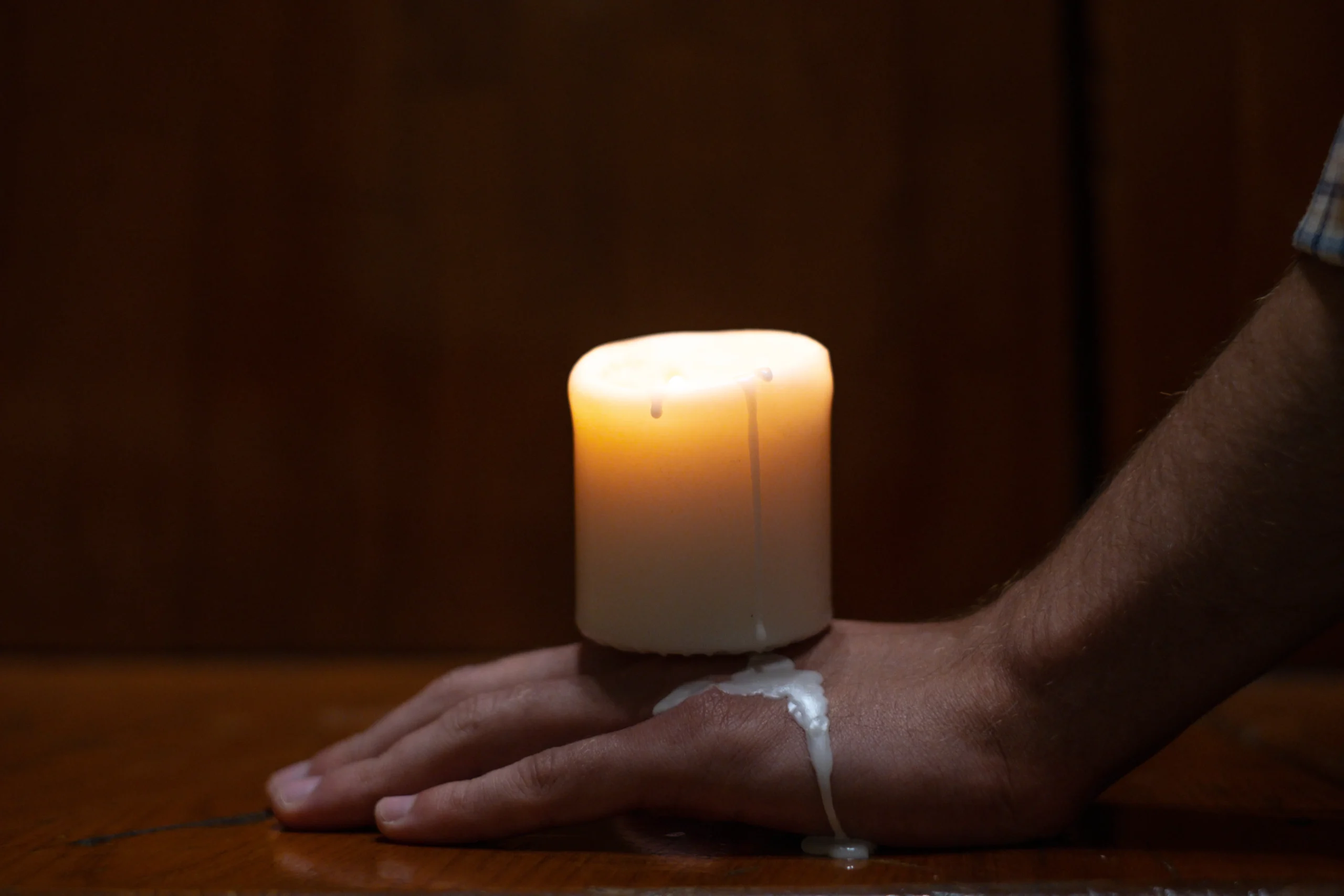 Melting wax from a lit candle dripping onto a person's hand.