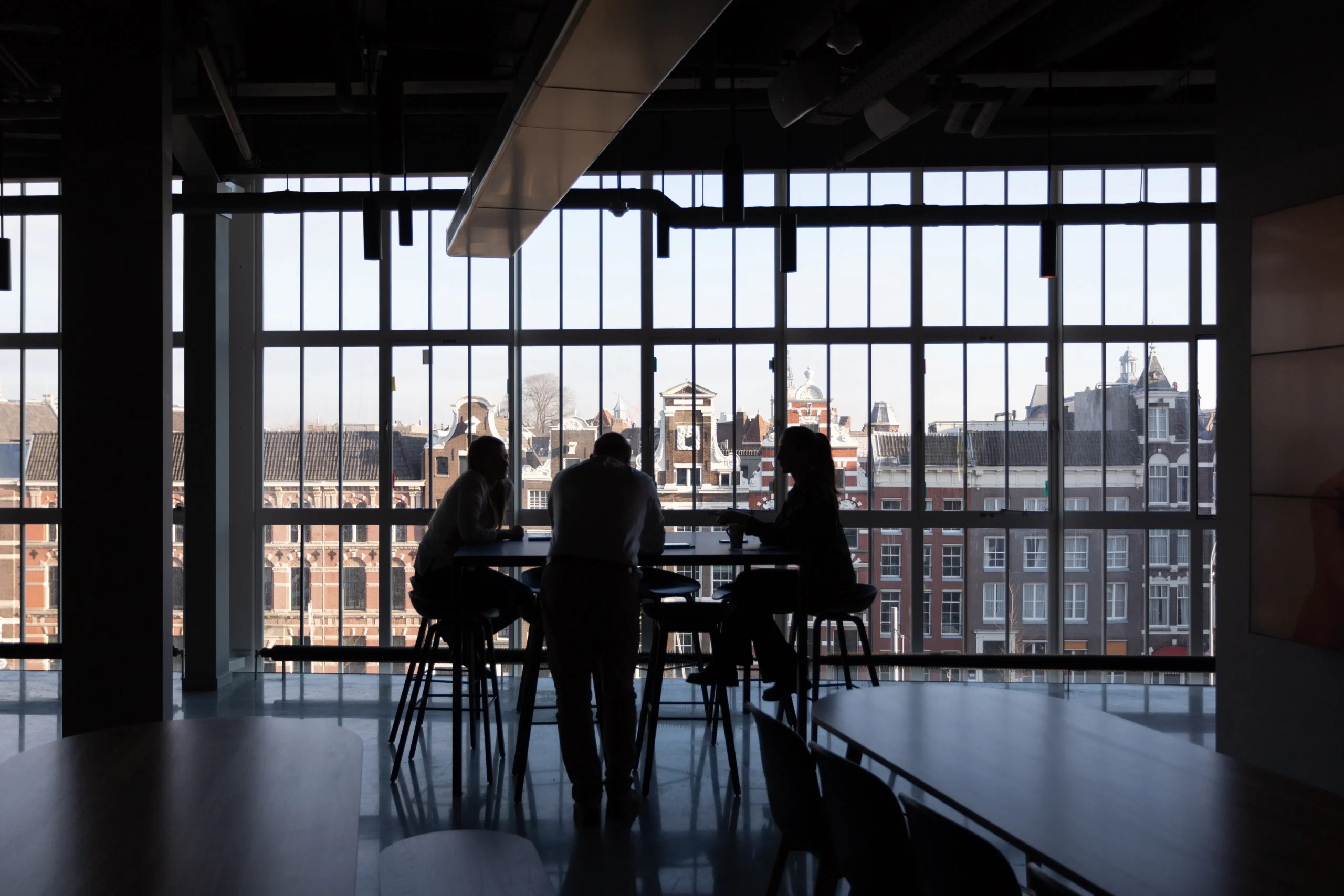 Silhouetted people by window overlooking Amsterdam cityscape.