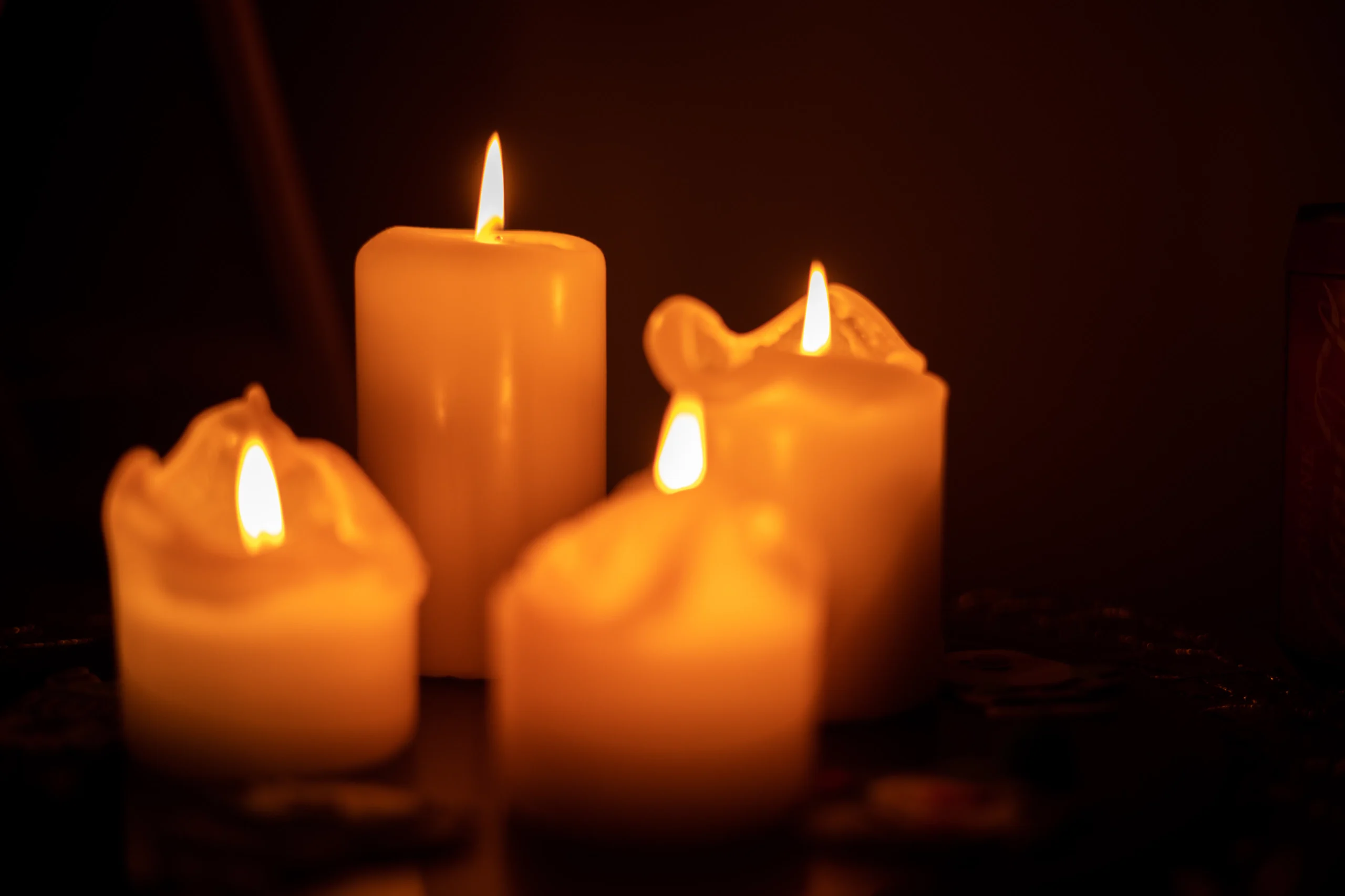 Four lit candles with flickering flames in a dark setting.
