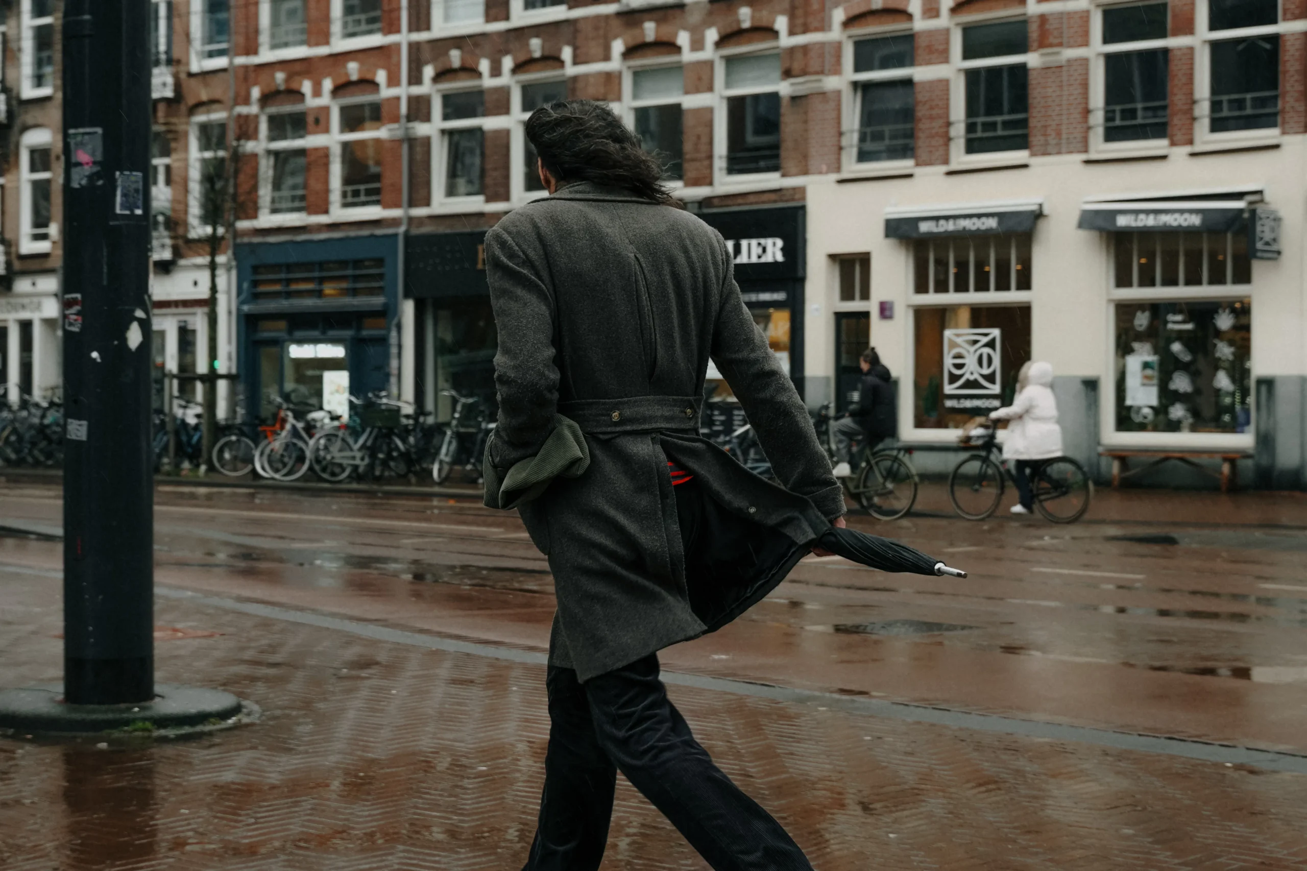 Person in a coat walking on a wet Amsterdam street with bicycles parked nearby.
