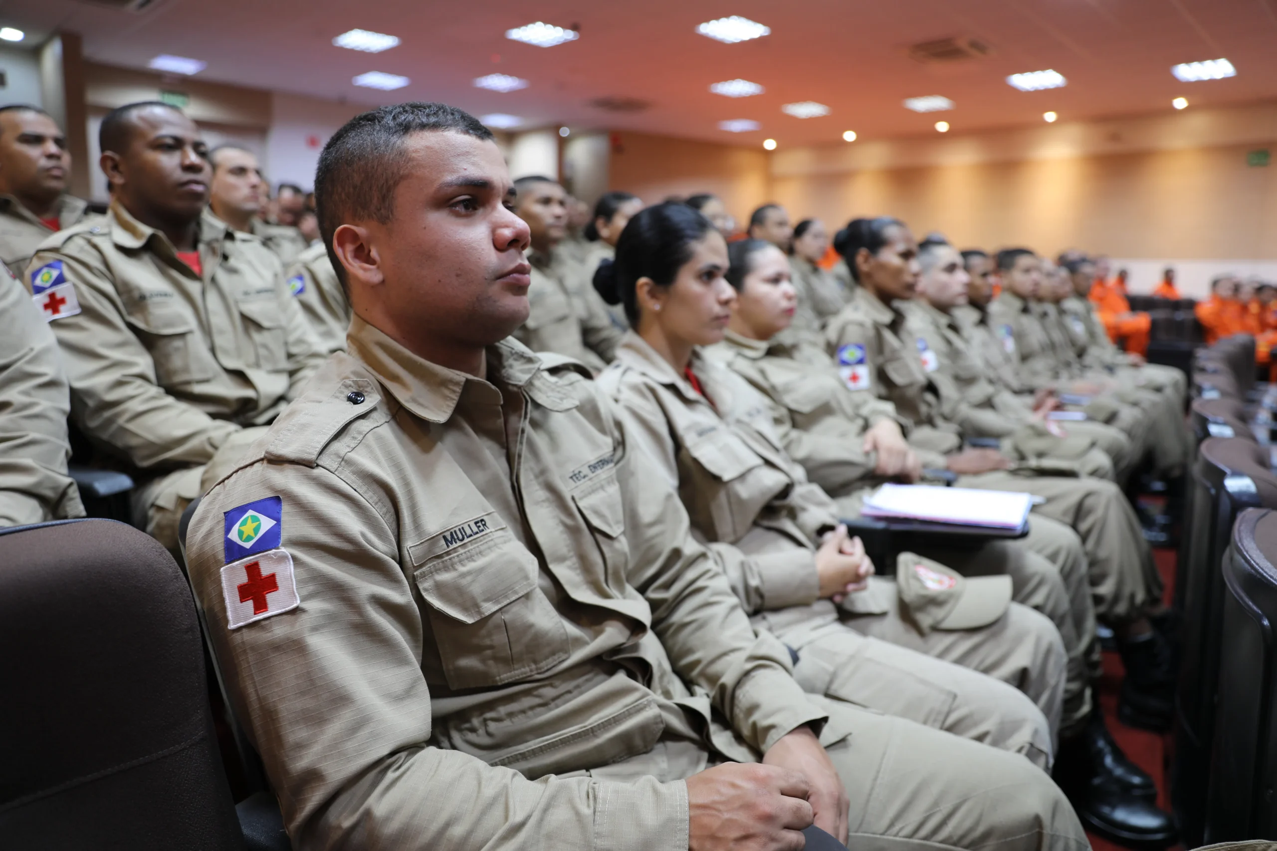 Rows of people in tan uniforms seated in an auditorium.