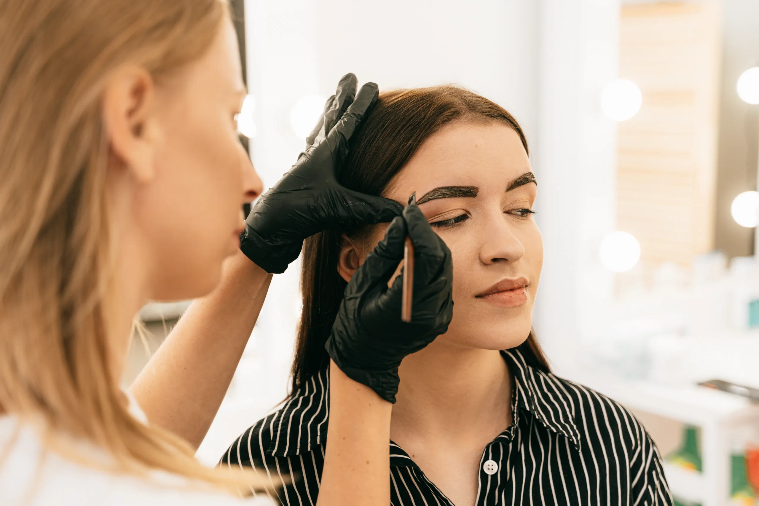 Esthetician shaping client's eyebrows with wax for eyebrow waxing service.