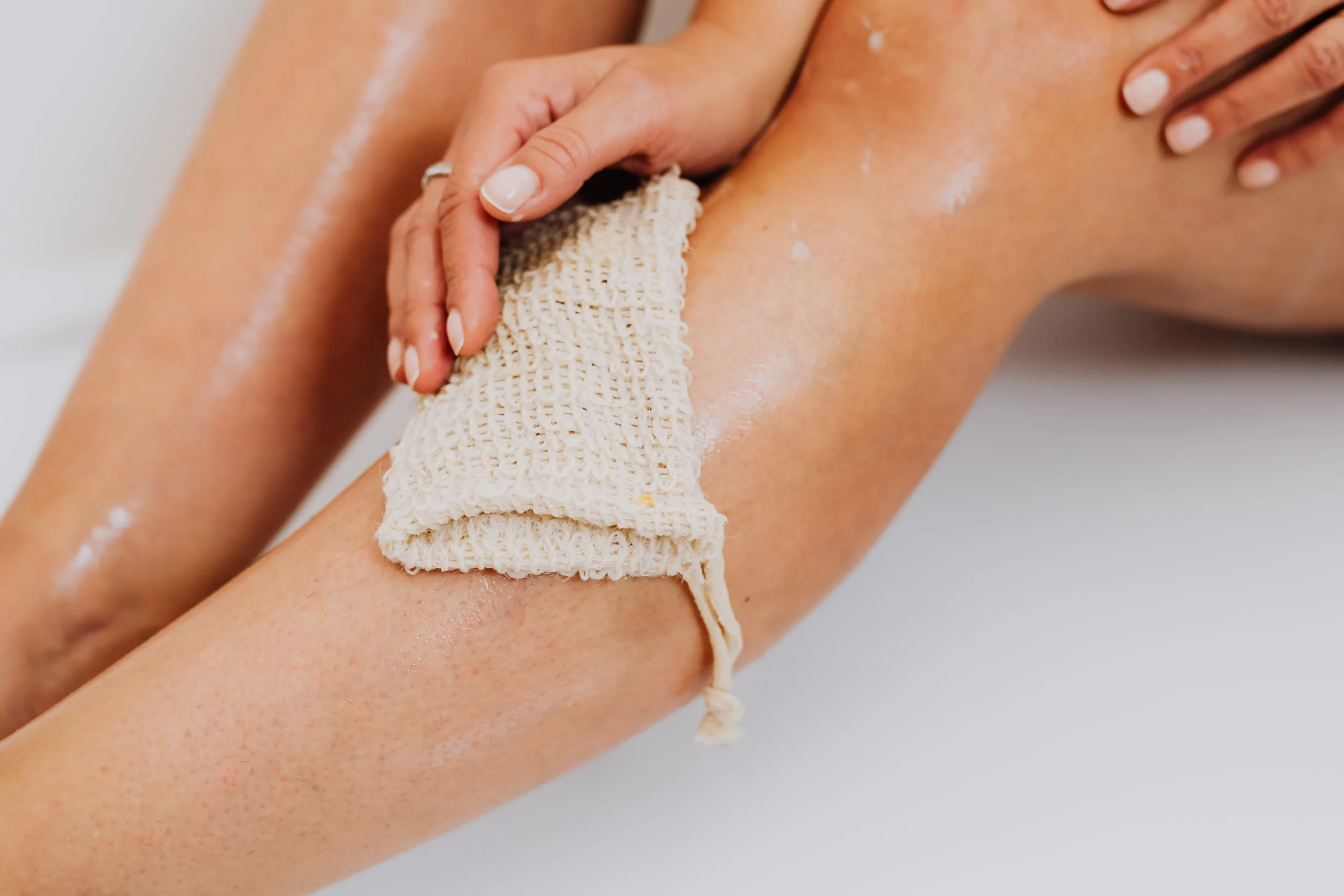 Woman exfoliating her smooth legs with a woven scrub mitt.