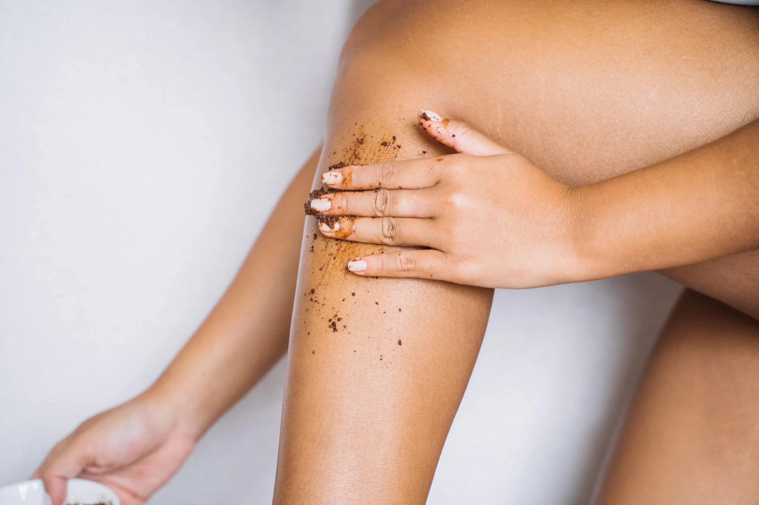 Woman exfoliating her leg with scrub to prepare for smooth legs and leg waxing.