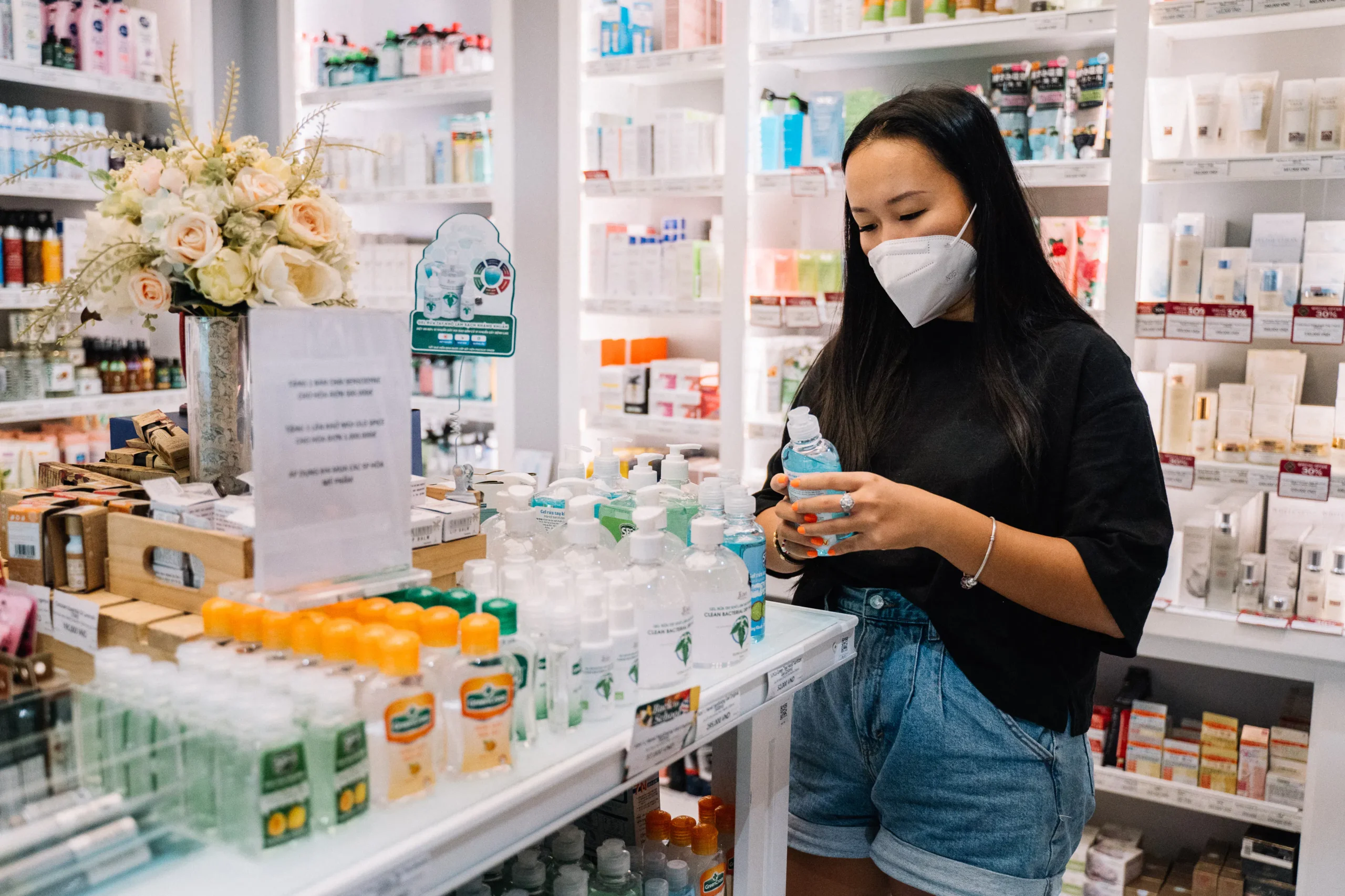 Woman in face mask examines lotion at an Amsterdam beauty salon shelf.