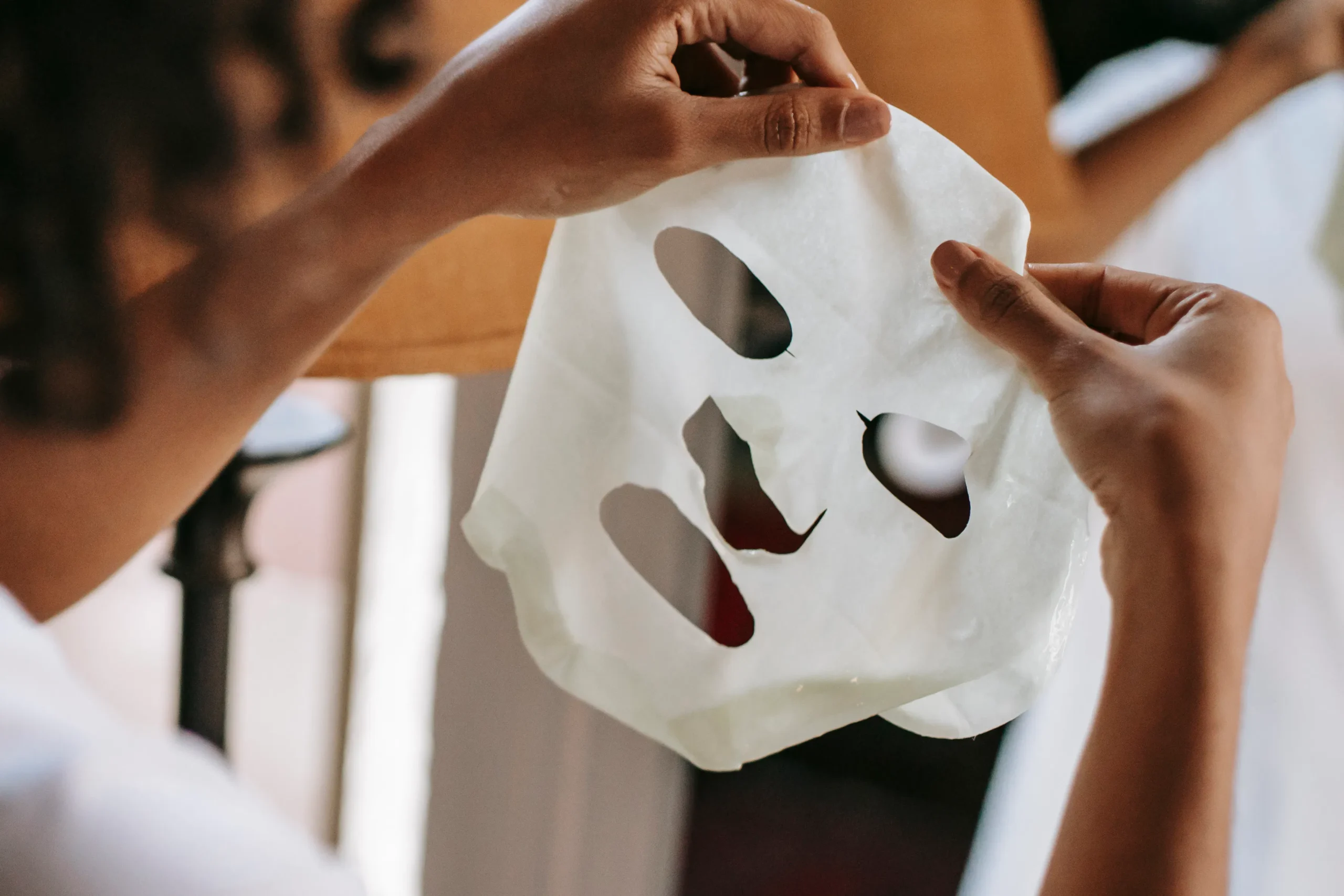 Person holding a white sheet mask with eye and mouth cutouts, preparing for silky skin.