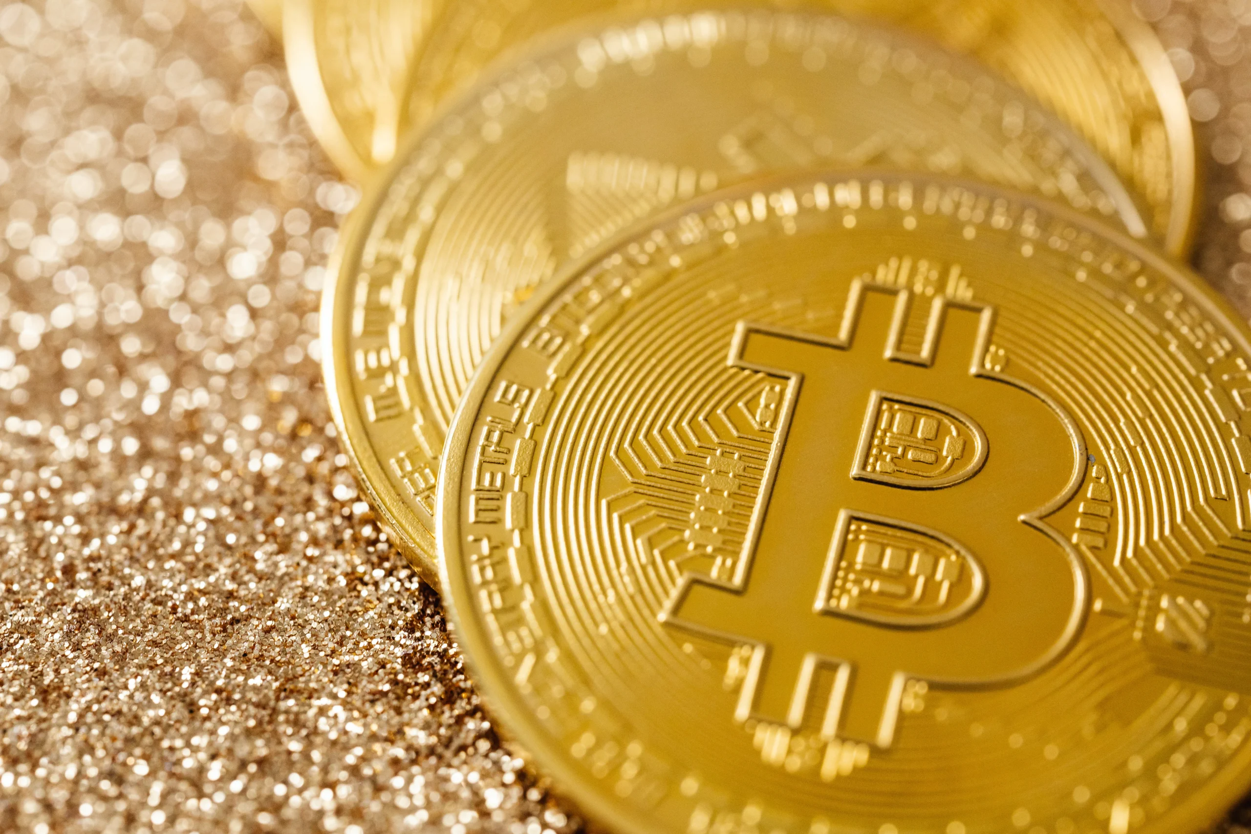 Close-up of shiny gold Bitcoin coins on a glittery gold surface.