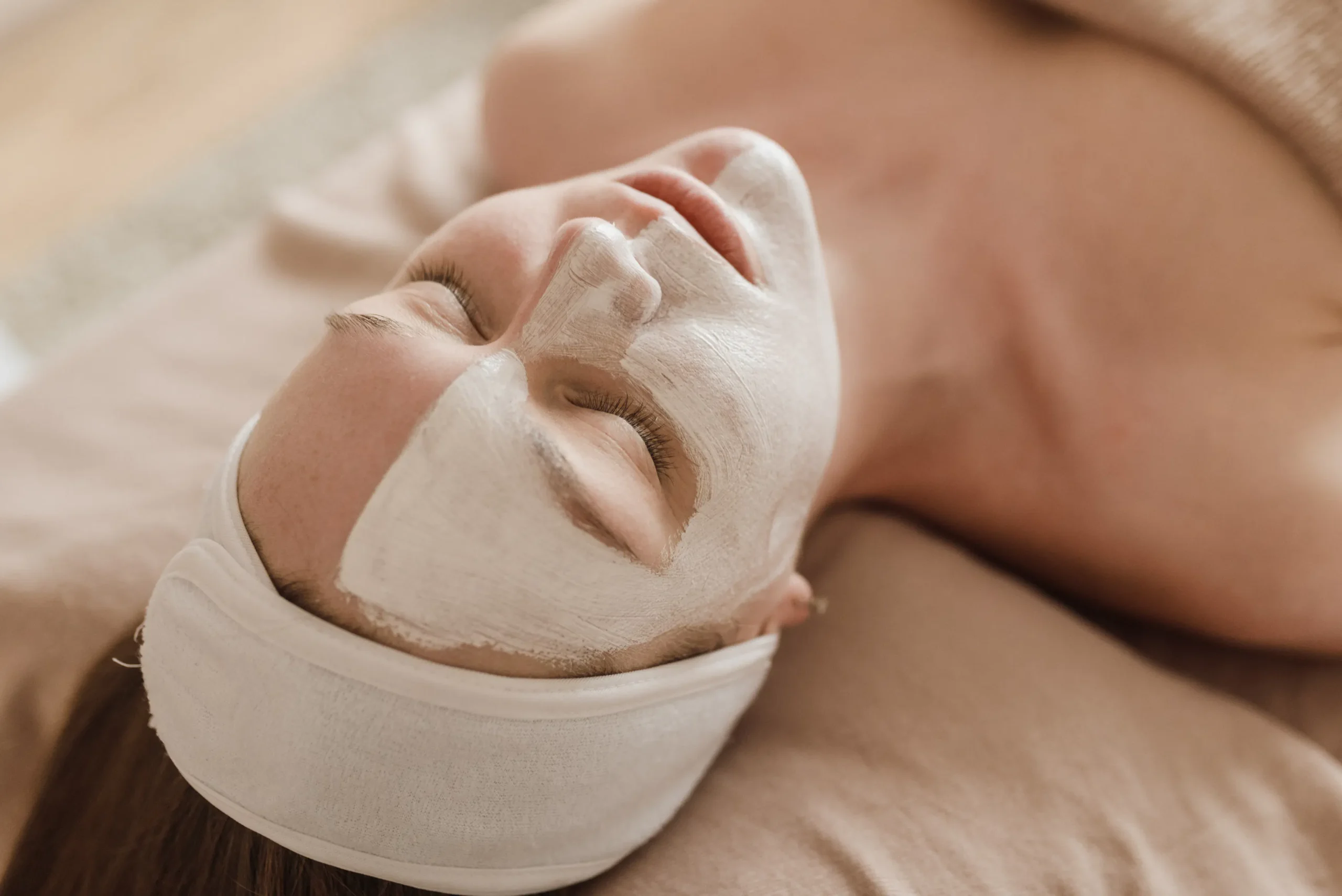 Woman with face mask and headband receiving skin treatment at an Amsterdam salon.
