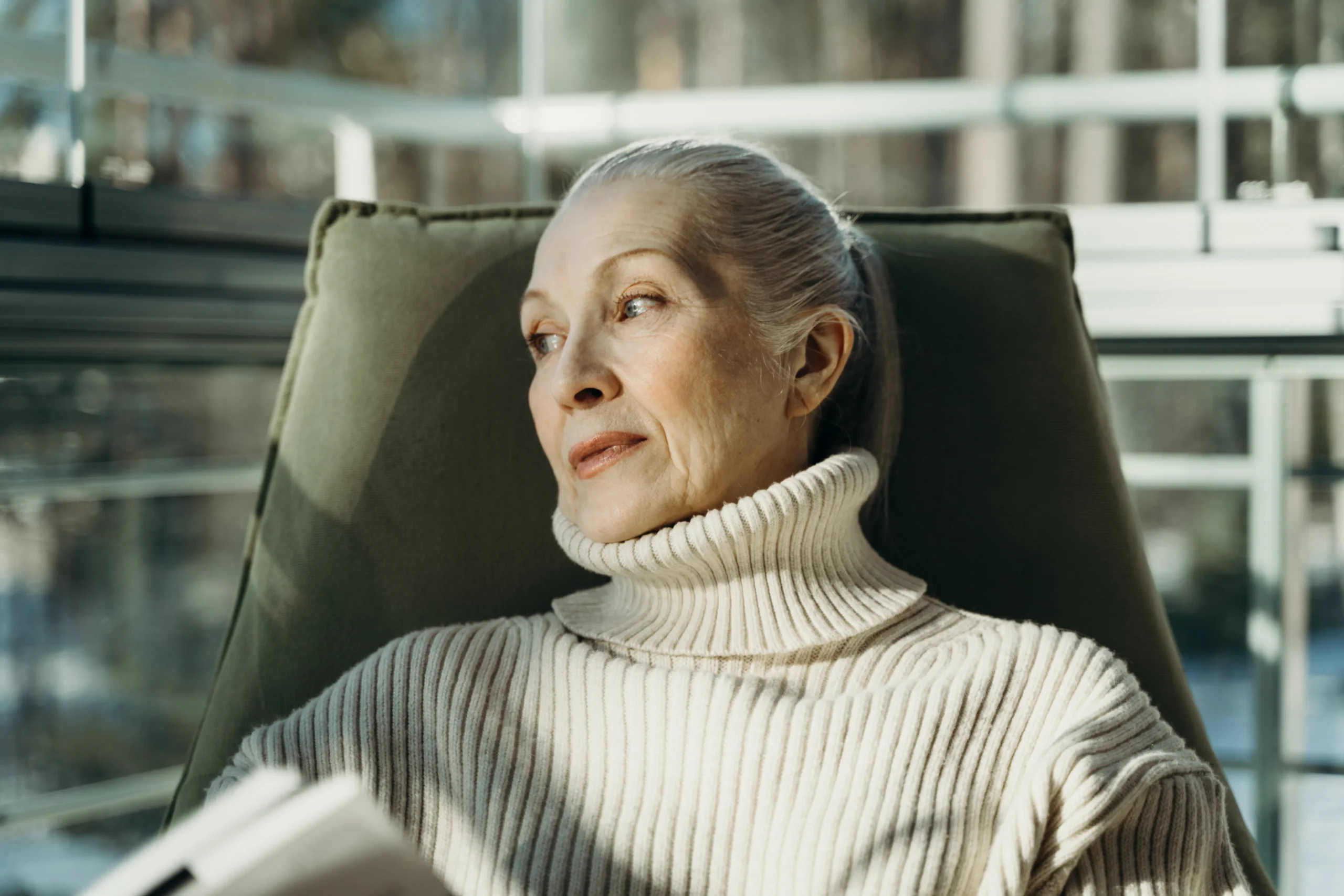 Woman in white turtleneck sweater sitting in a chair by the window