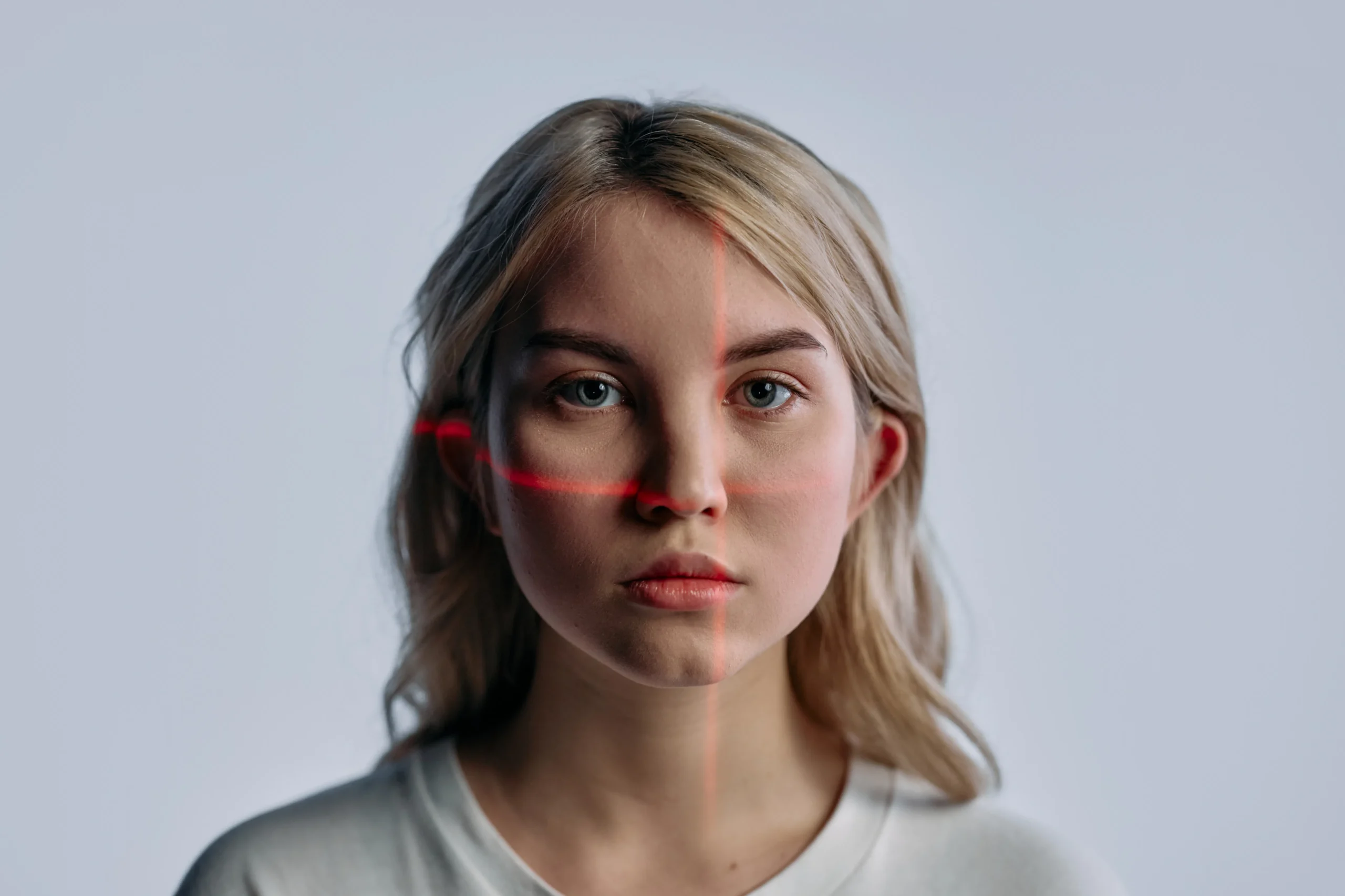 Blonde woman's face with red laser lines for facial laser treatment hair reduction.