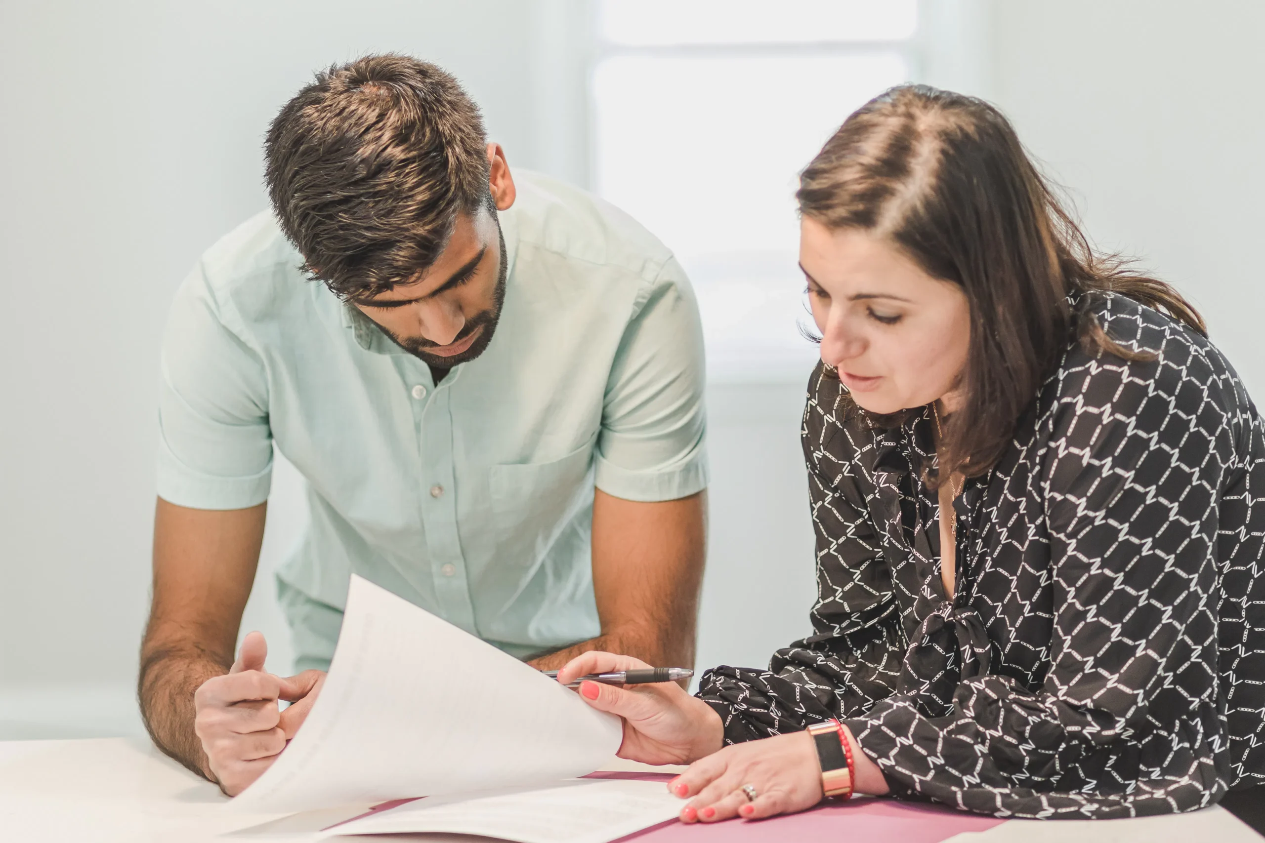 Two professionals reviewing documents at a bright table, discussing details.
