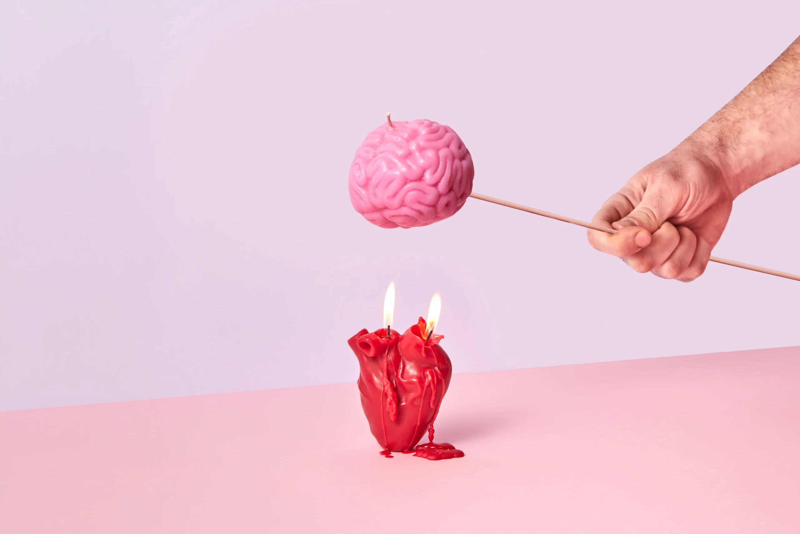 Hand holding a pink brain-shaped object above heart-shaped candles.