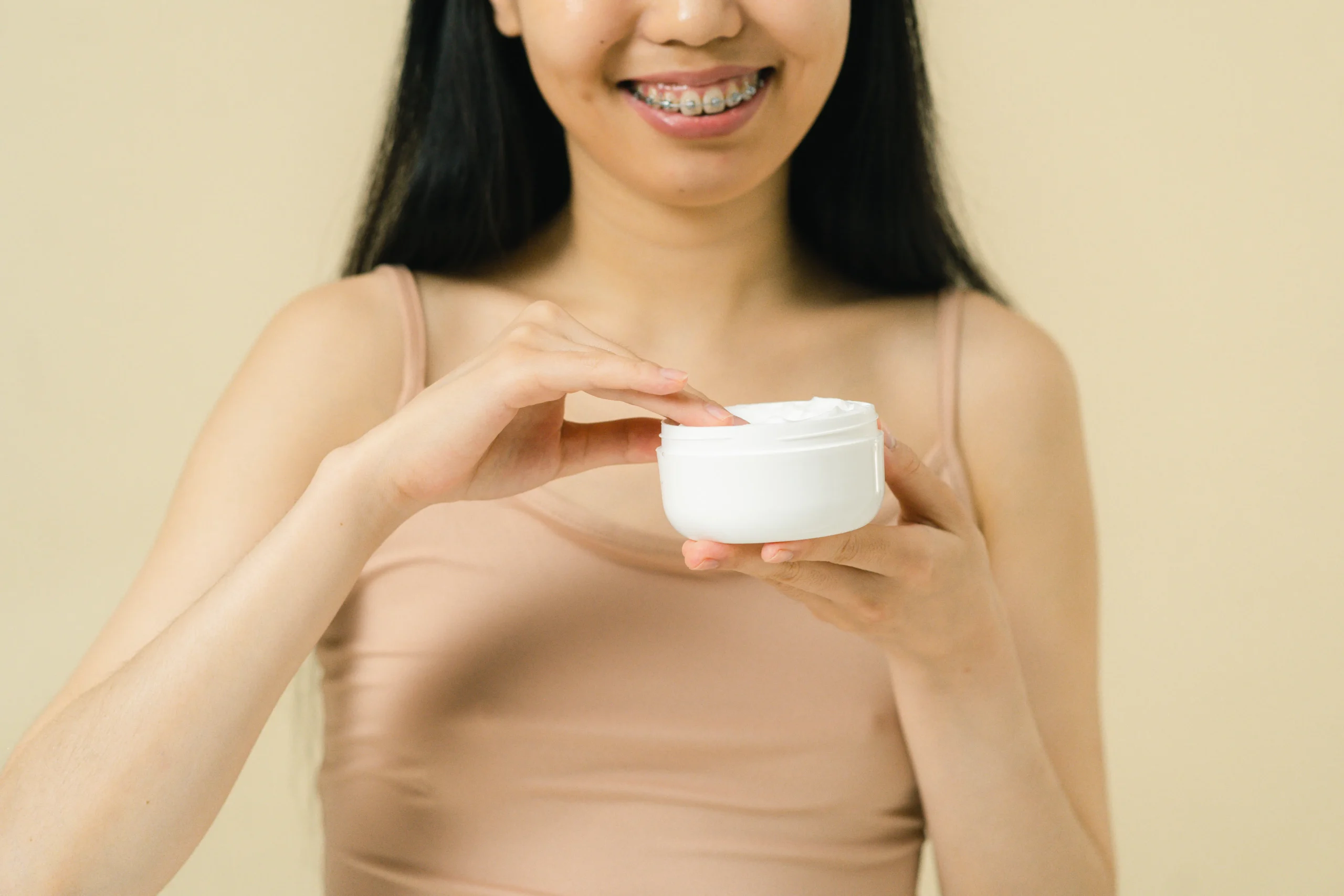 Teenager with braces applying facial cream after professional waxing treatment.