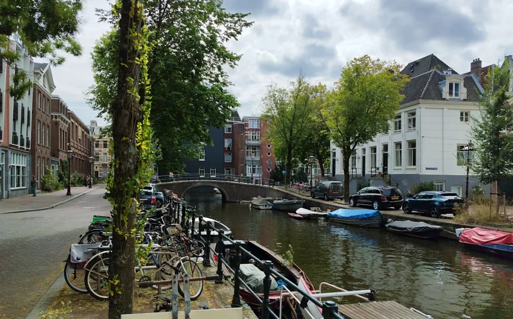 Amsterdam canal view with parked bikes and boats on the water.