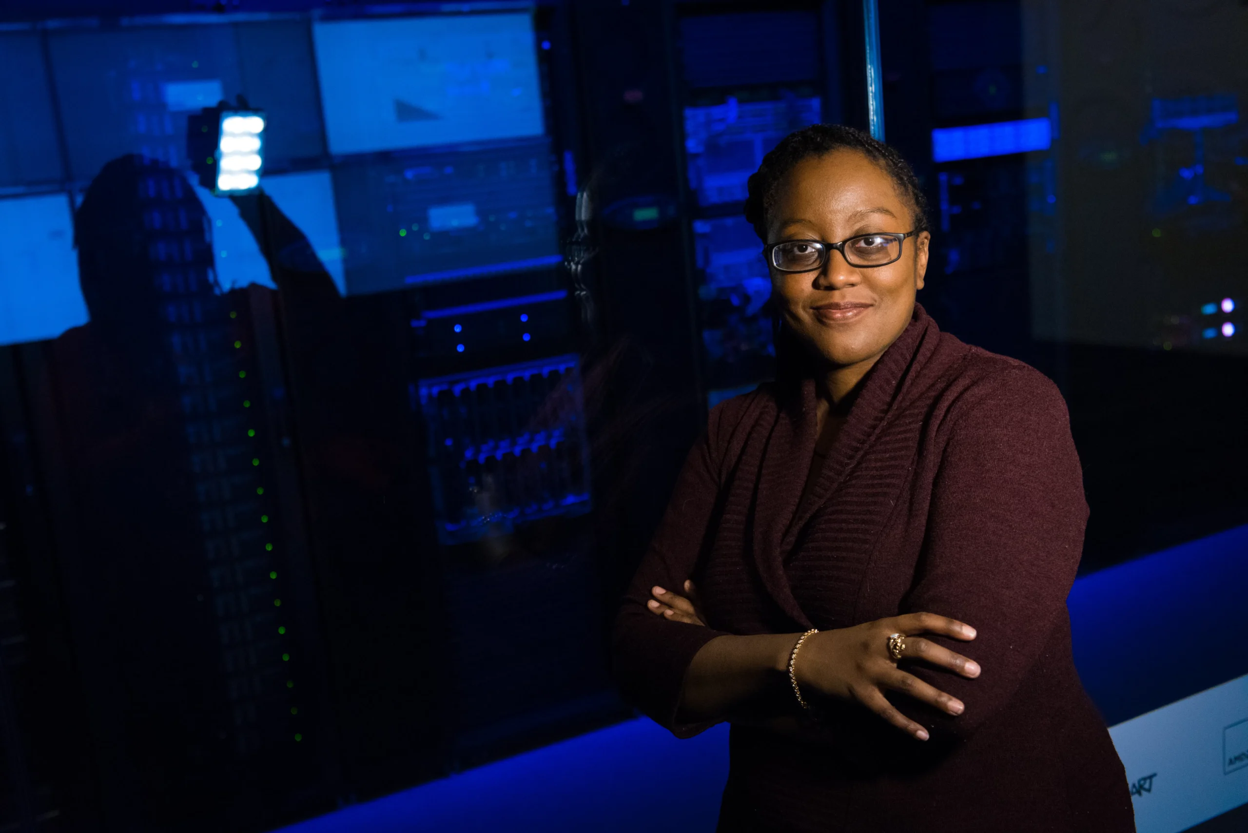 Woman with glasses standing in front of a blue-lit server room.