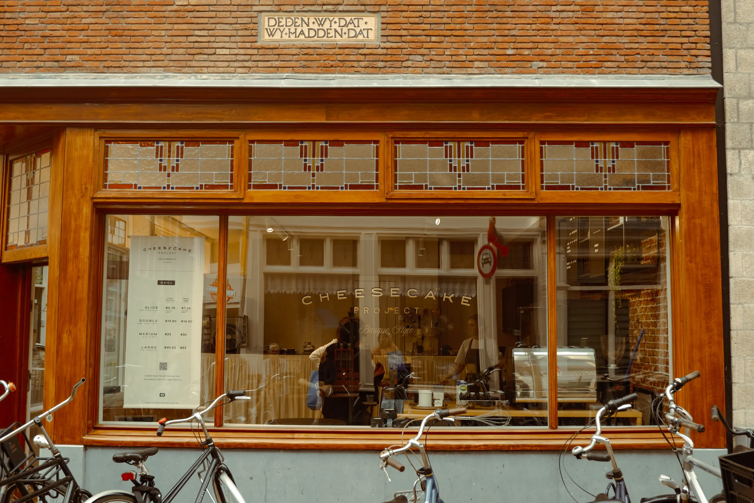 Cheesecake shop window in Amsterdam with bikes parked outside.
