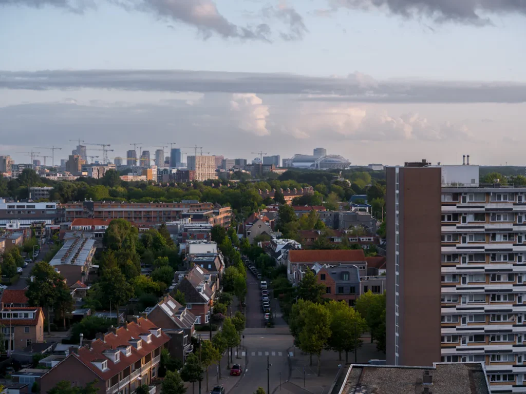 Amsterdam cityscape with modern buildings and residential areas under cloudy sky.