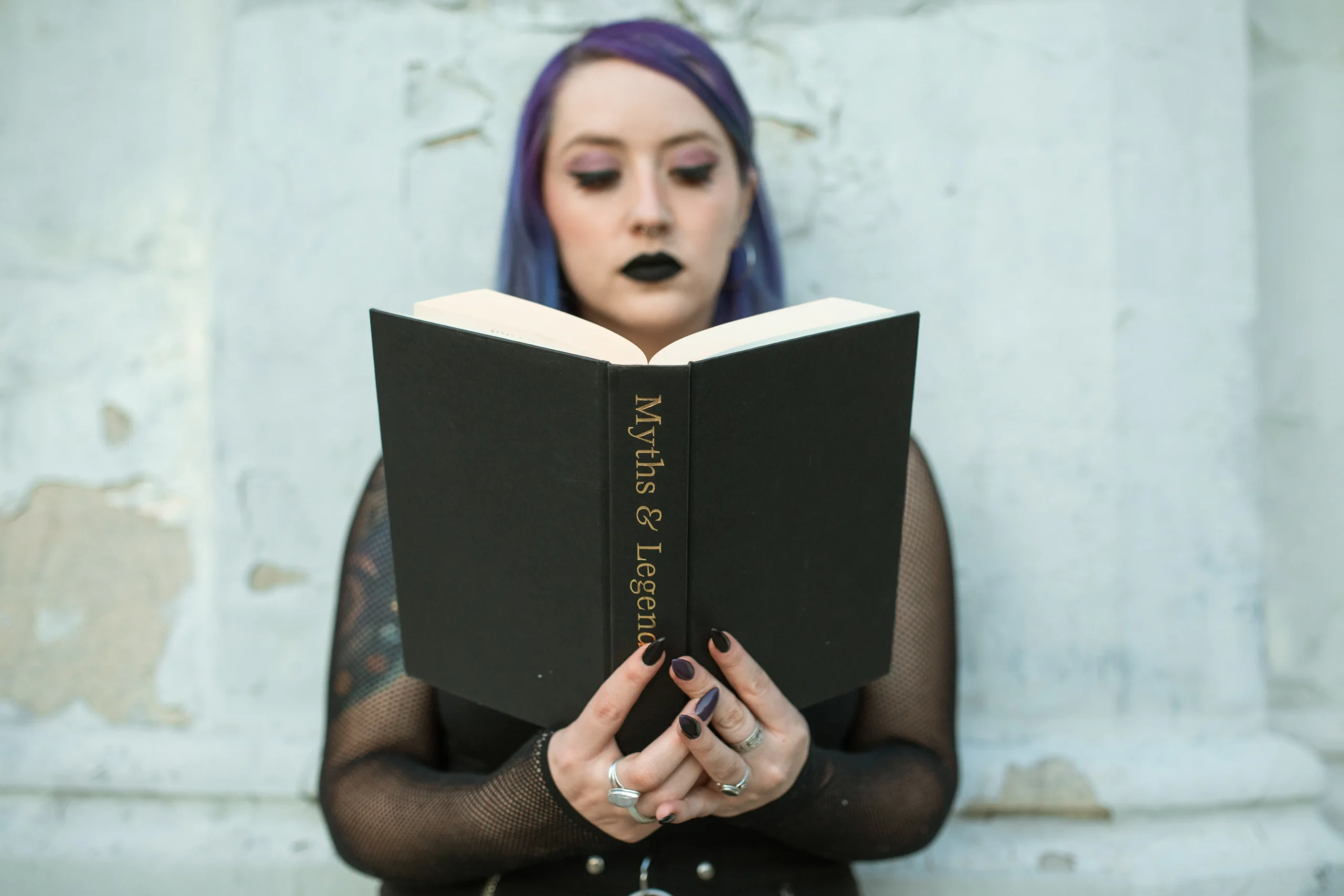 Woman with purple hair reading a book titled 'Myths & Legends'.