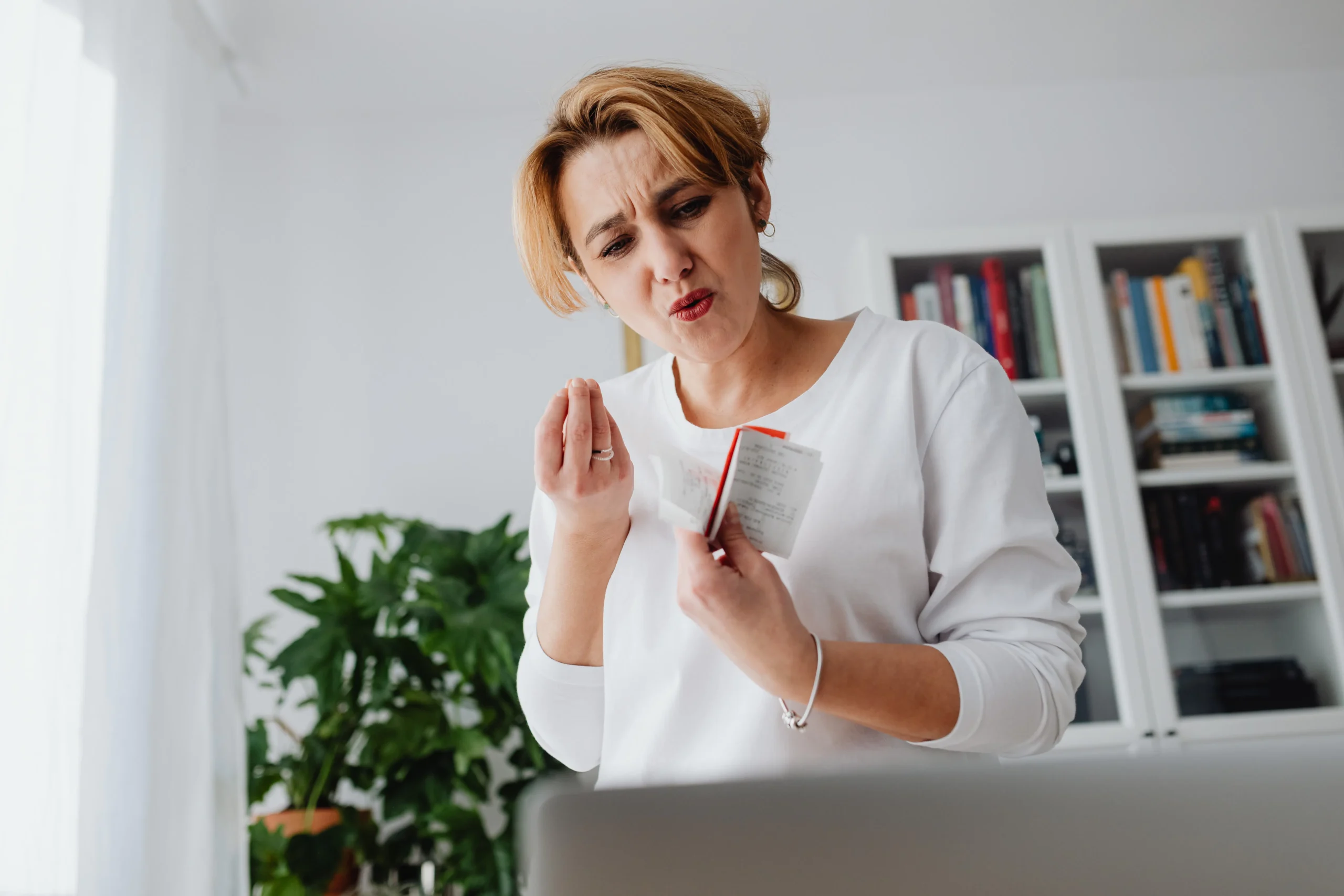 Woman looking skeptically at a receipt or bill in a notebook indoors.