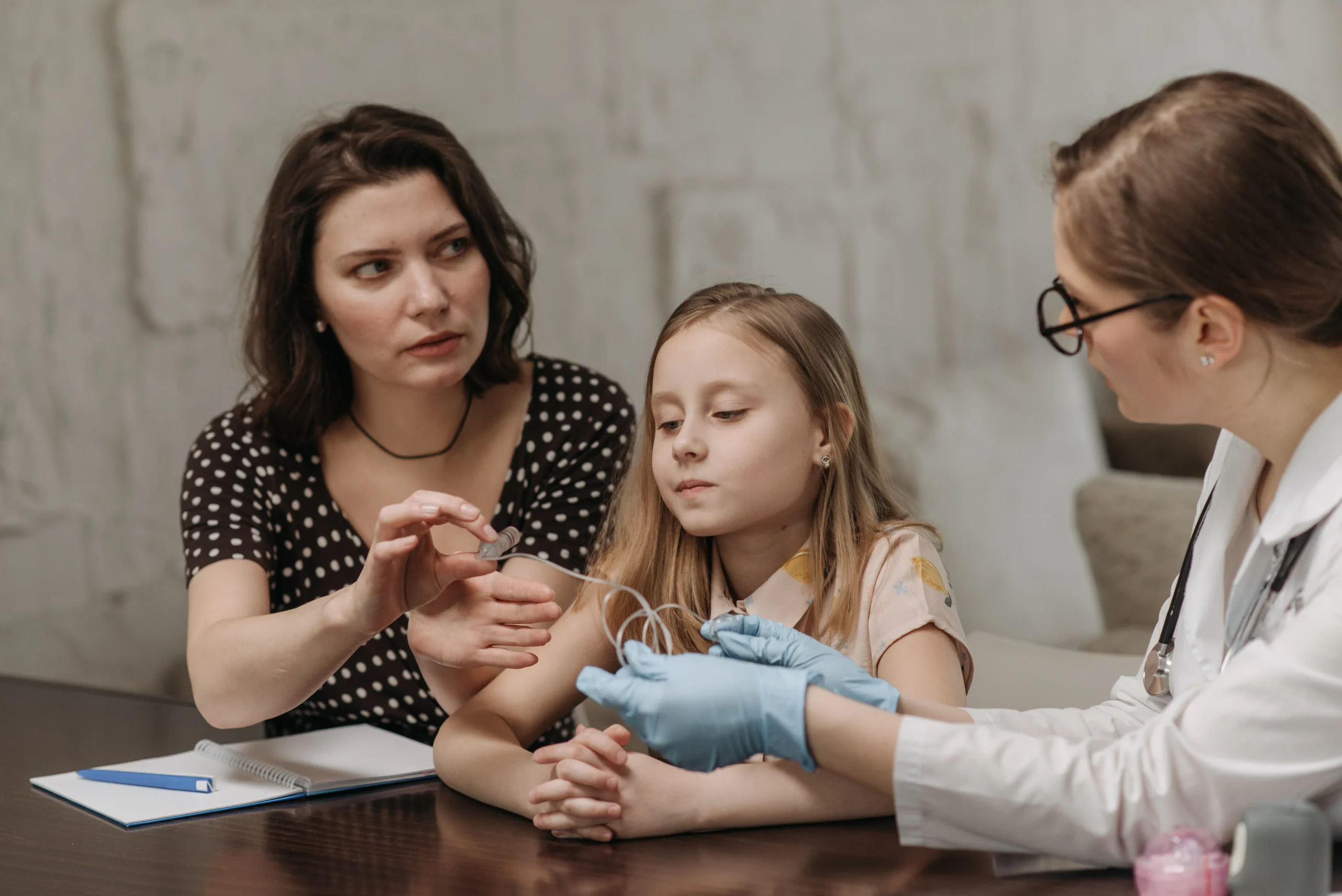 Doctor examining child's arm with mother present in medical setting.