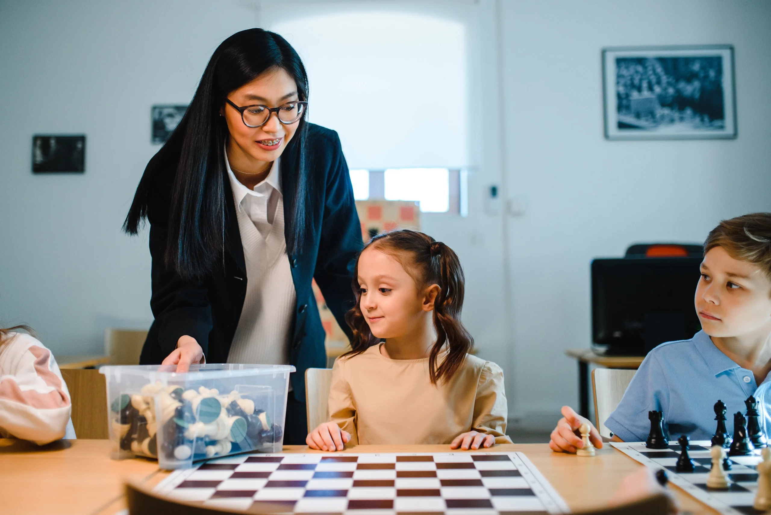 Teacher with students playing chess at a table.