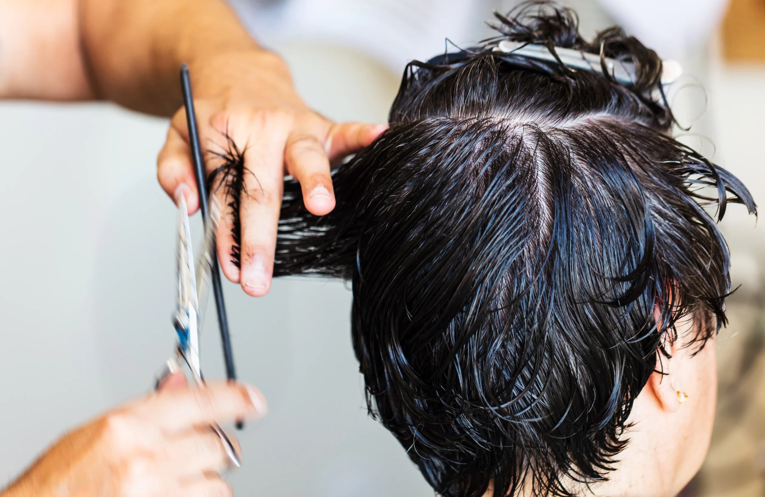 Professional hairdresser's hands meticulously cutting a client's wet dark hair, emphasizing a quality hair cut and salon experience in Amsterdam.