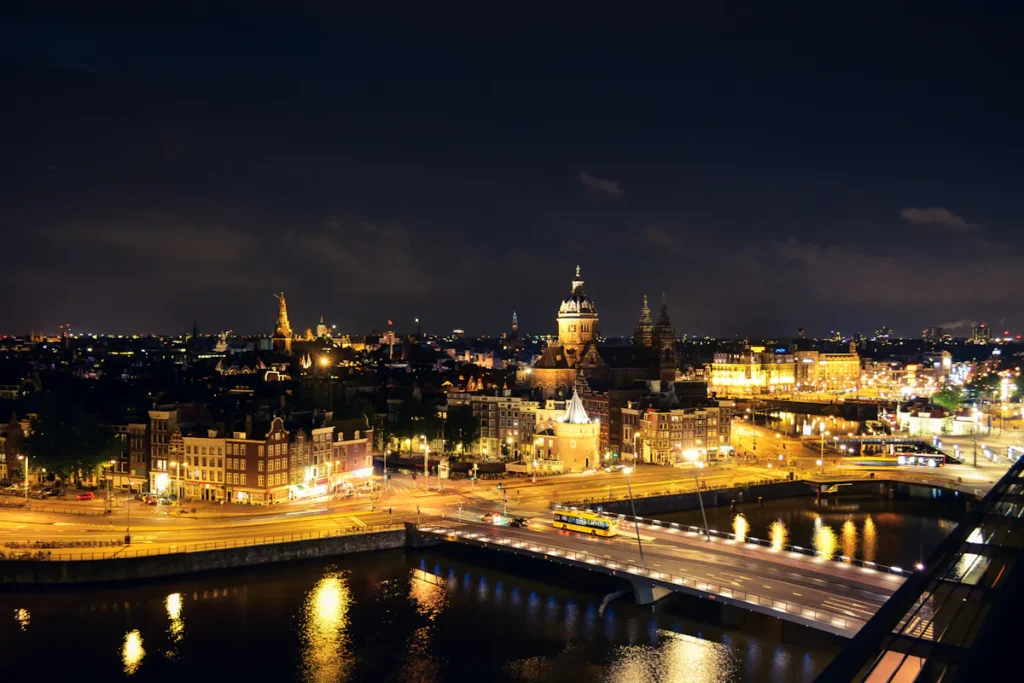 Night view of Amsterdam, bridges and buildings illuminated with golden lights reflecting on the water.
