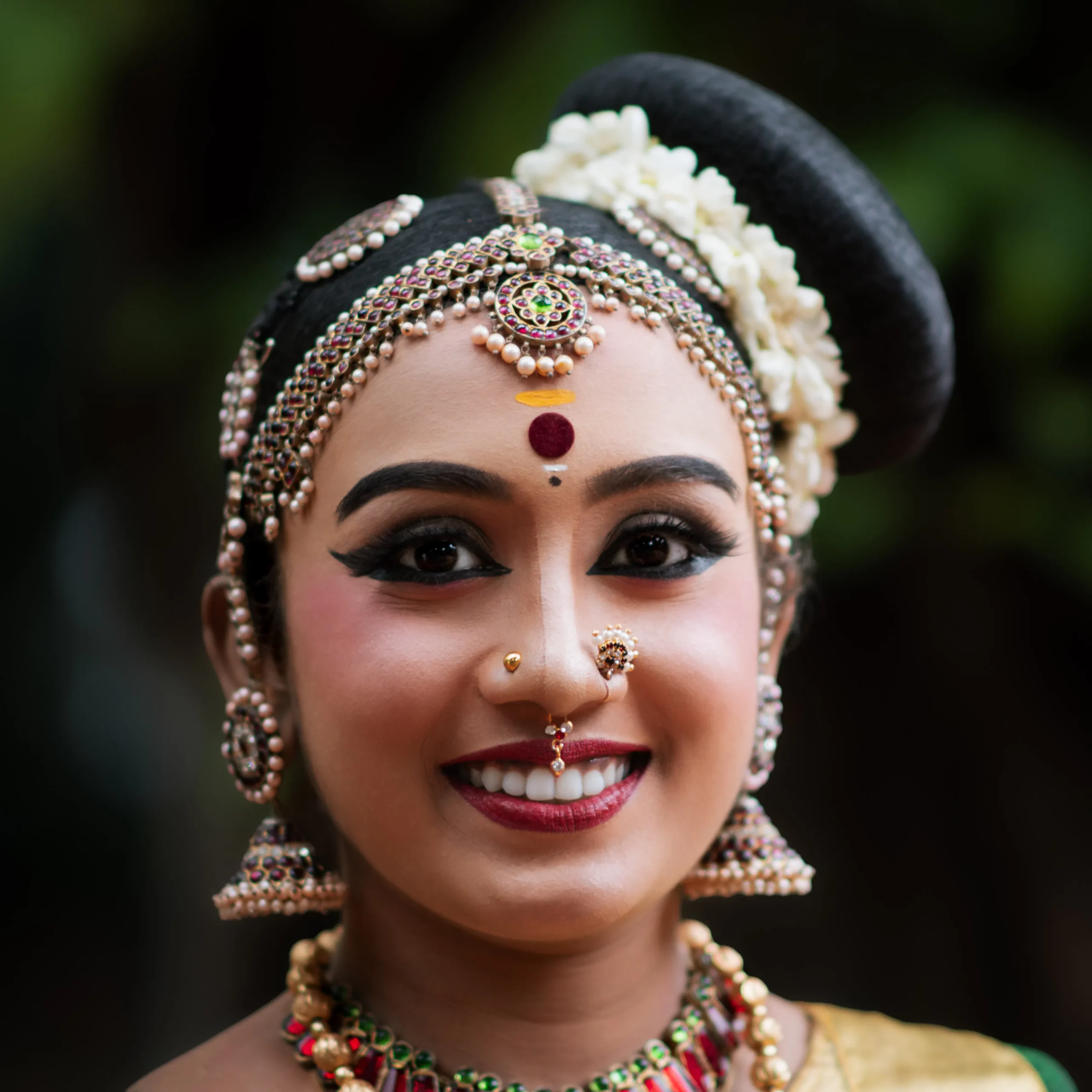 Close-up of smiling woman wearing traditional Indian Bharatanatyam dance makeup and jewelry.
