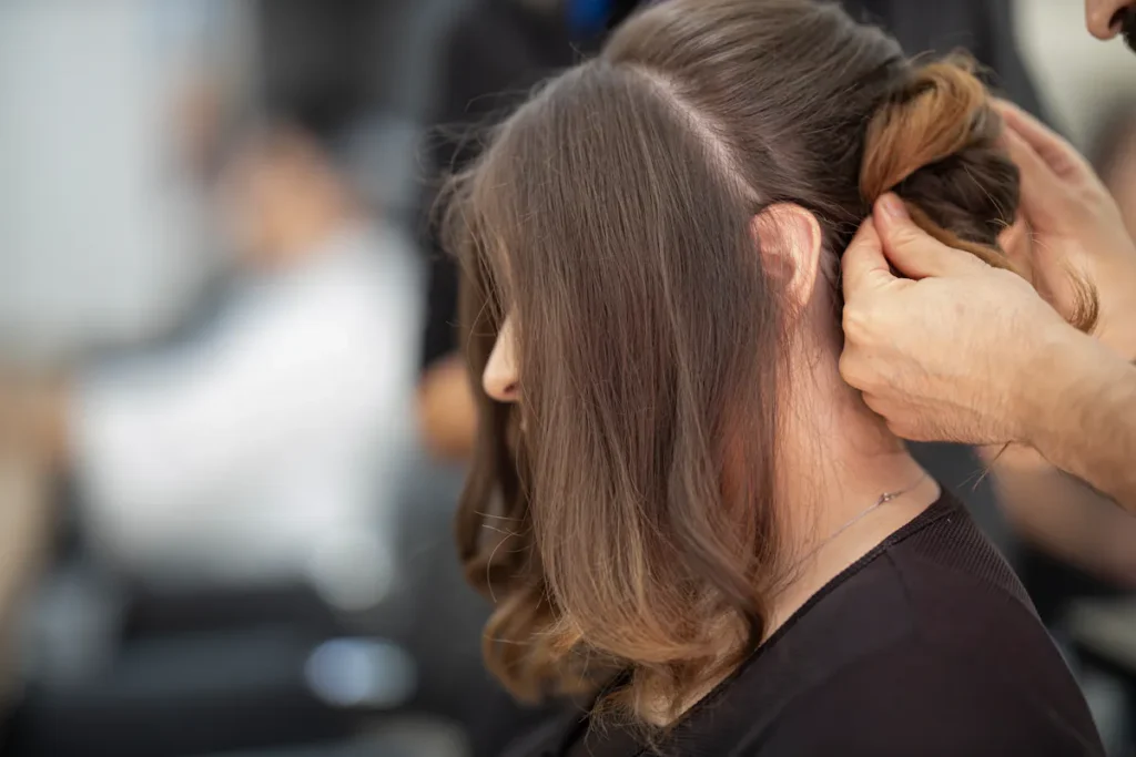 Stylist arranging long brown hair at Amsterdam beauty salon; getting professional beauty services.