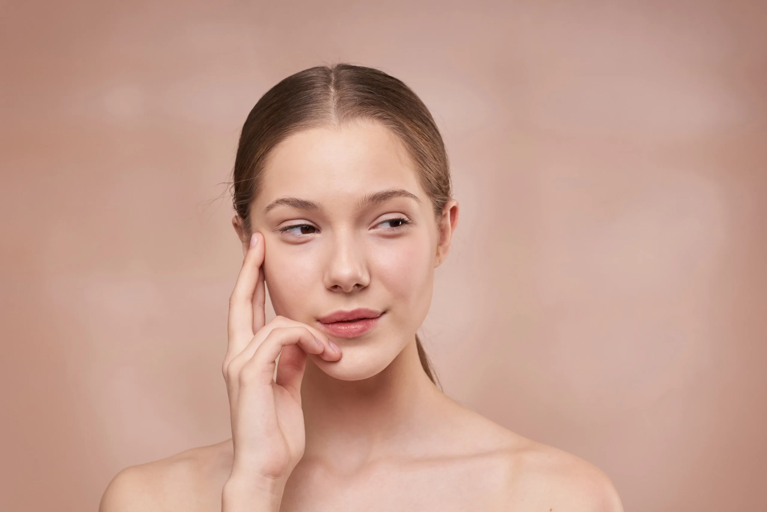 Close-up of a young woman with clear, healthy skin, gently touching her face, representing