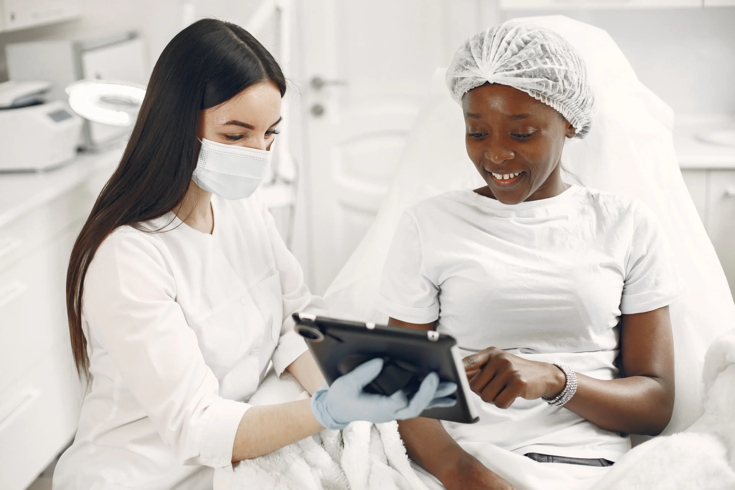 Aesthetician in a mask and gloves shows a tablet to a smiling client, likely discussing carbon peeling results or other facial treatment options for skin rejuvenation in Amsterdam.
