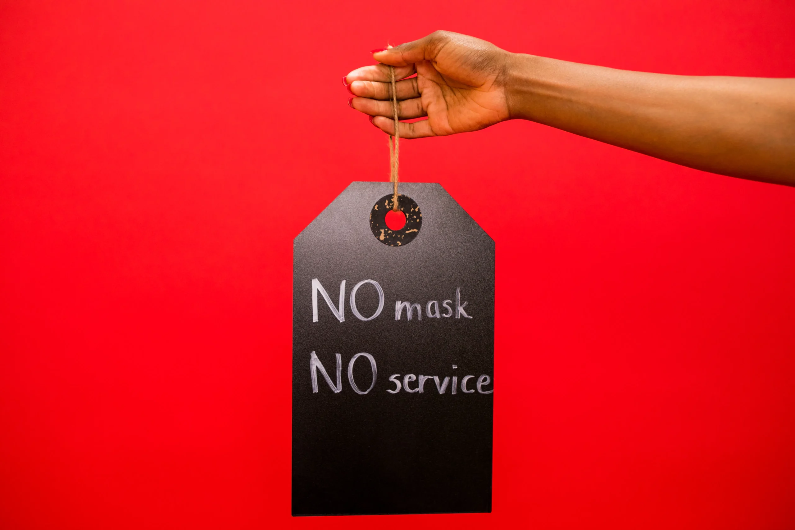 Hand holding sign reading 'No mask, no service' against a red background.